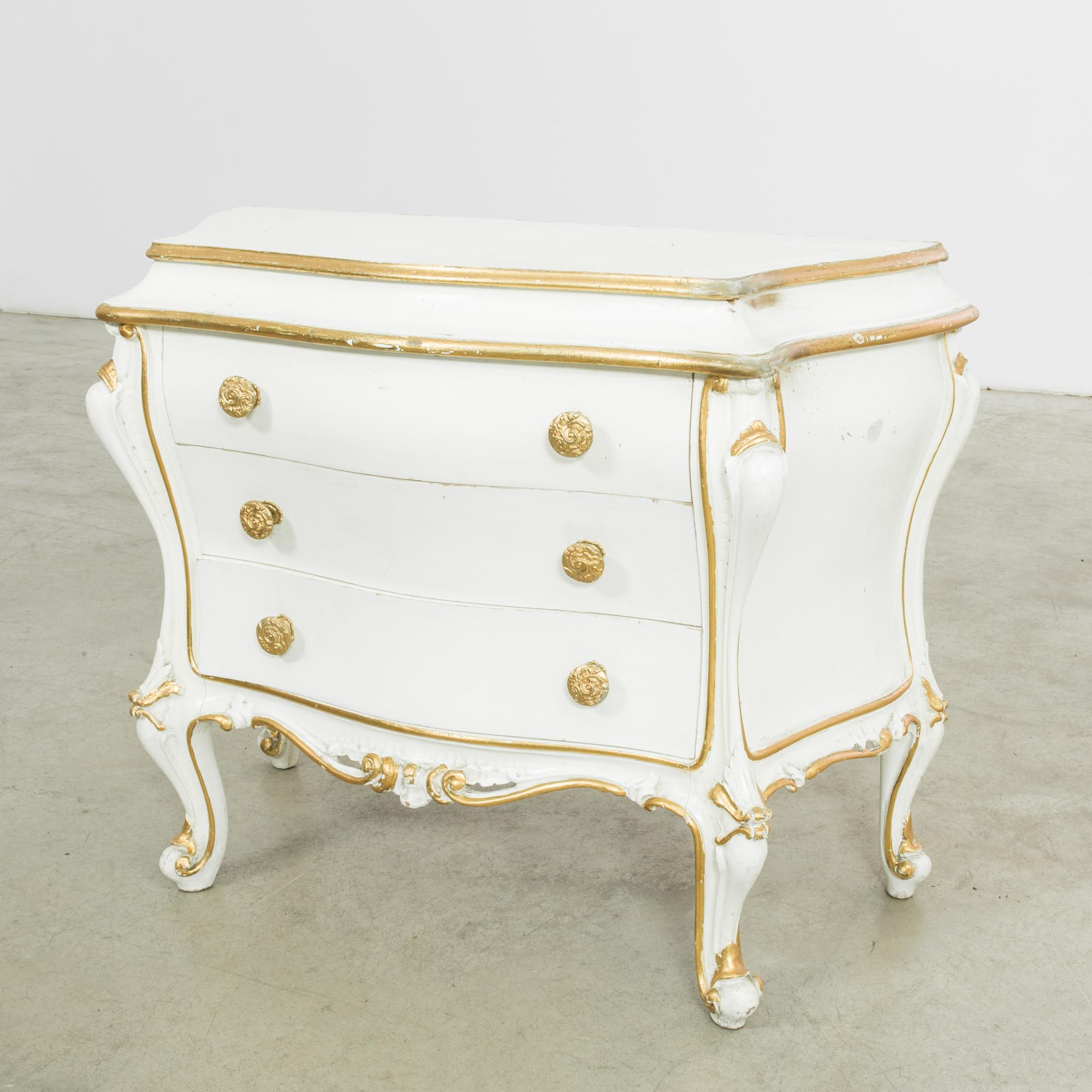Elevate your space with the timeless allure of this 1960s Italian white patinated wooden chest of drawers. Radiating an air of elegance, the base is finished in a pristine white, accentuated by opulent gold accents meticulously gracing every inch.