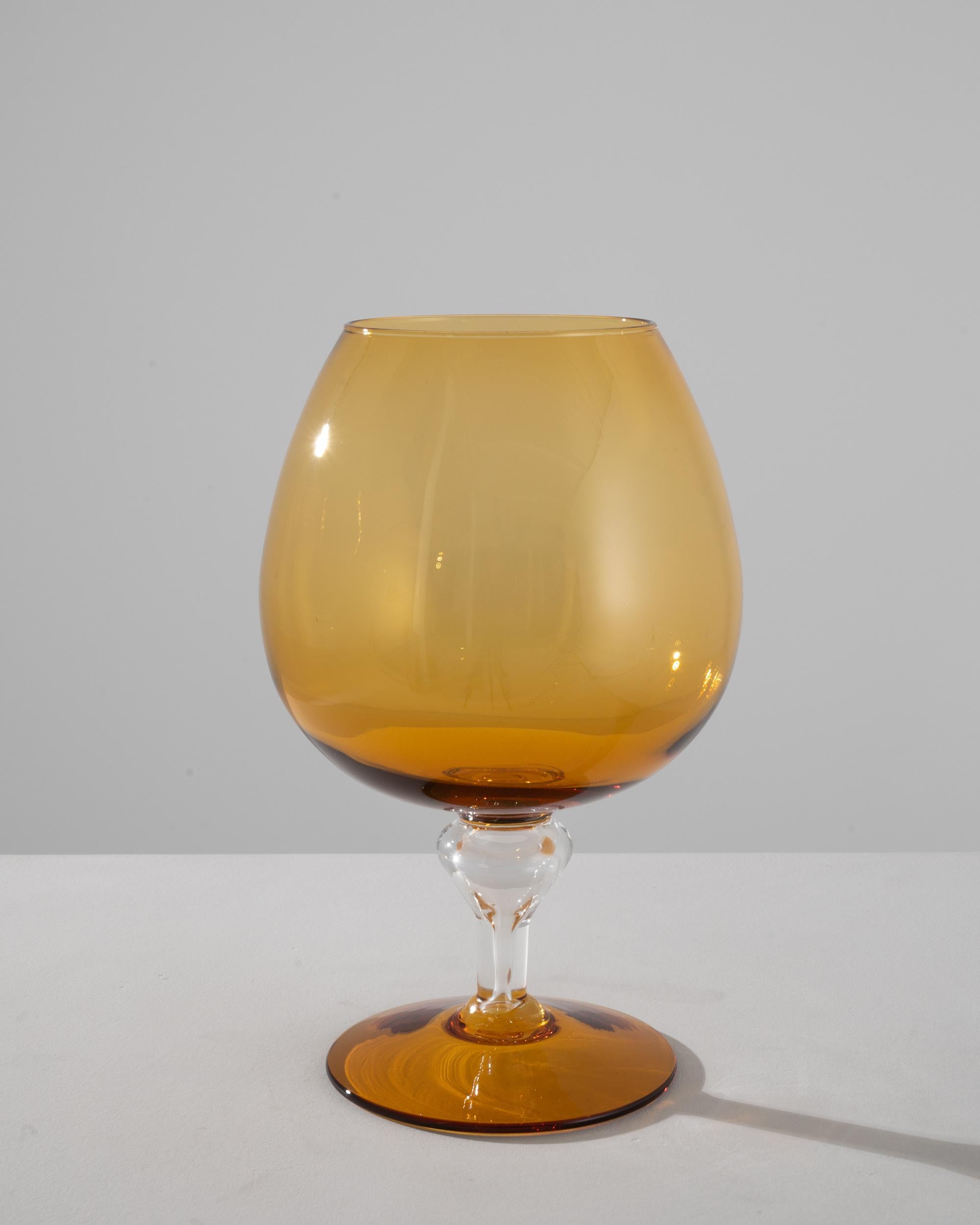 This 1960s Italian yellow glass goblet is a stunning example of vintage craftsmanship. The amber-colored glass, with its soft, sun-kissed glow, brings warmth to any room. The goblet's bowl is generous in size, elegantly rising from a beautifully