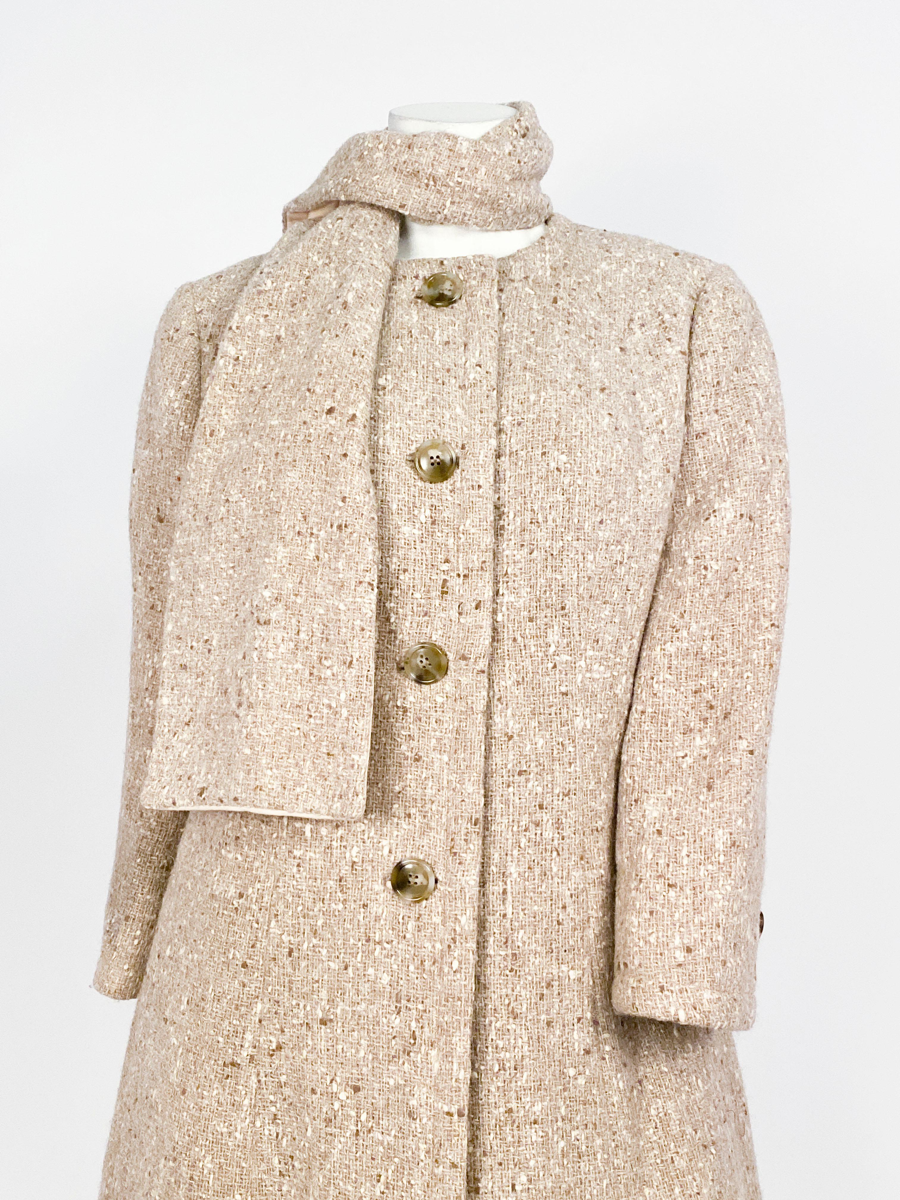 1960s Jean Louis three-piece suit (coat, skirt, & scarf) set made of a beige tweed with specks of lighter and darker tones. The coat and the skirt has an A-line silhouette and the suit is finished with a matching neck scarf.  