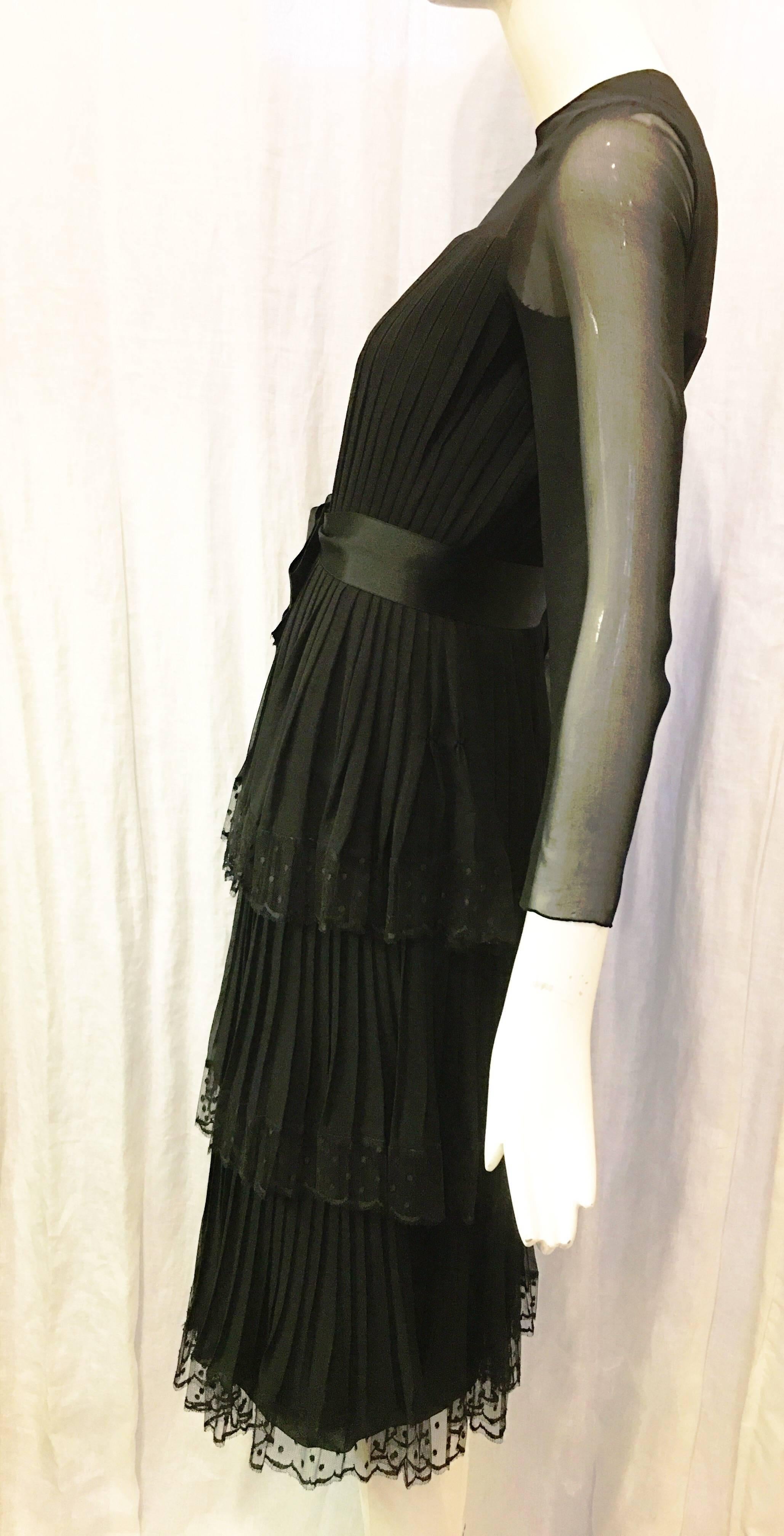 Black silk dress with sheer sleeves lace trim and waist bow belt detail. Bow belt closes at front with snap button and hook and eye closure. Dress is fully lined. Bottom of dress is tiered with three tiers, each of which is trimmed with lace. A