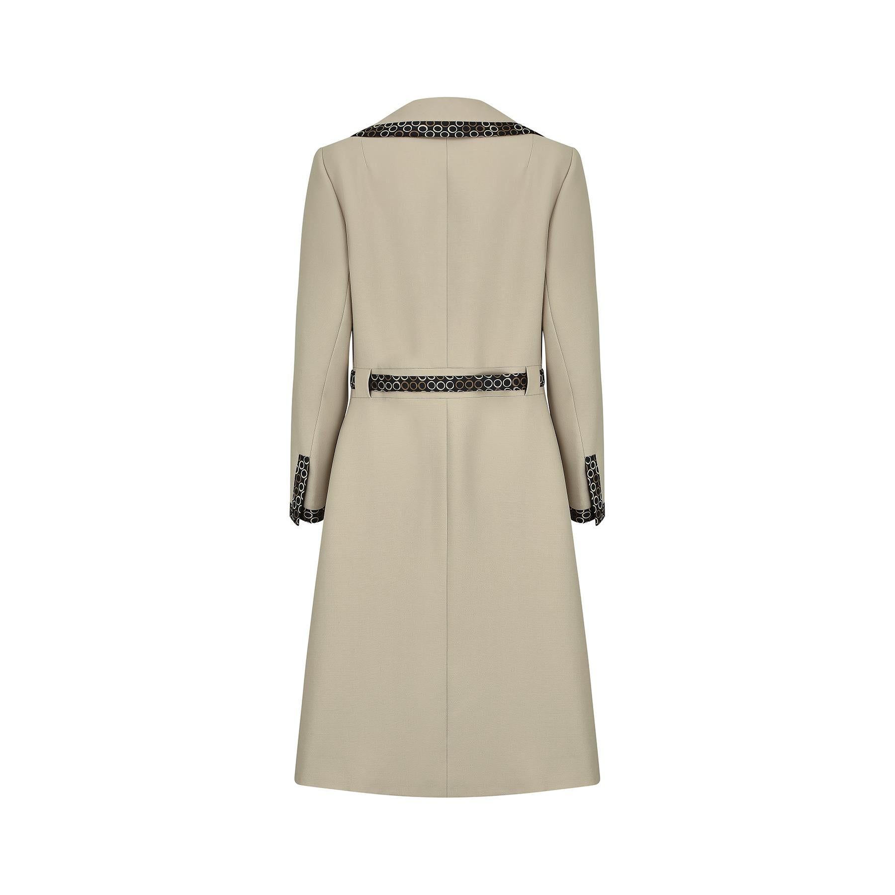 This is a very late 1960s or 1970 Jean Patou pale taupe coloured gabardine coat with the tailored in London label.  It has a stylish double-cut lapel and striking geometric circular pattern silk twill trim that runs along all the edges.  The fabric