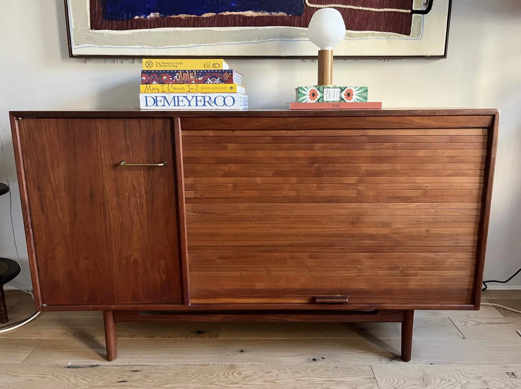 Jens Risom Teak Credenza with a stained solid teak frame and teak tambour door. Original brass hardware at the cabinet door and original teak hardware on the tambour door. Interior shelving throughout. This piece is in good condition with some wear