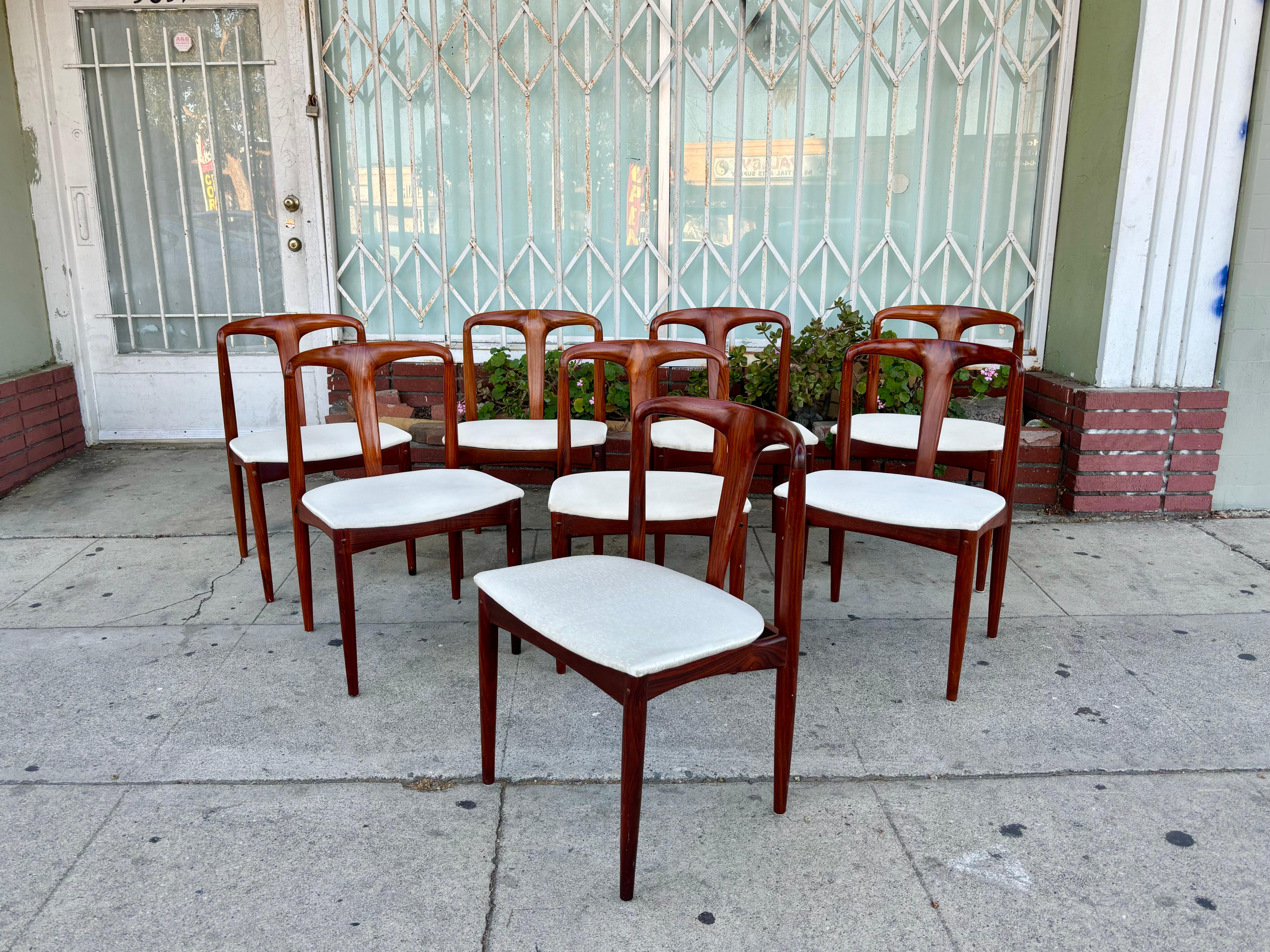 Danish modern rosewood dining chairs designed by Johannes Andersen and manufactured by Uldum Møbelfabrik in Denmark circa 1960s. These dining chairs feature a white fabric upholstery that sits on top of an amazing rosewood frame. What sets these