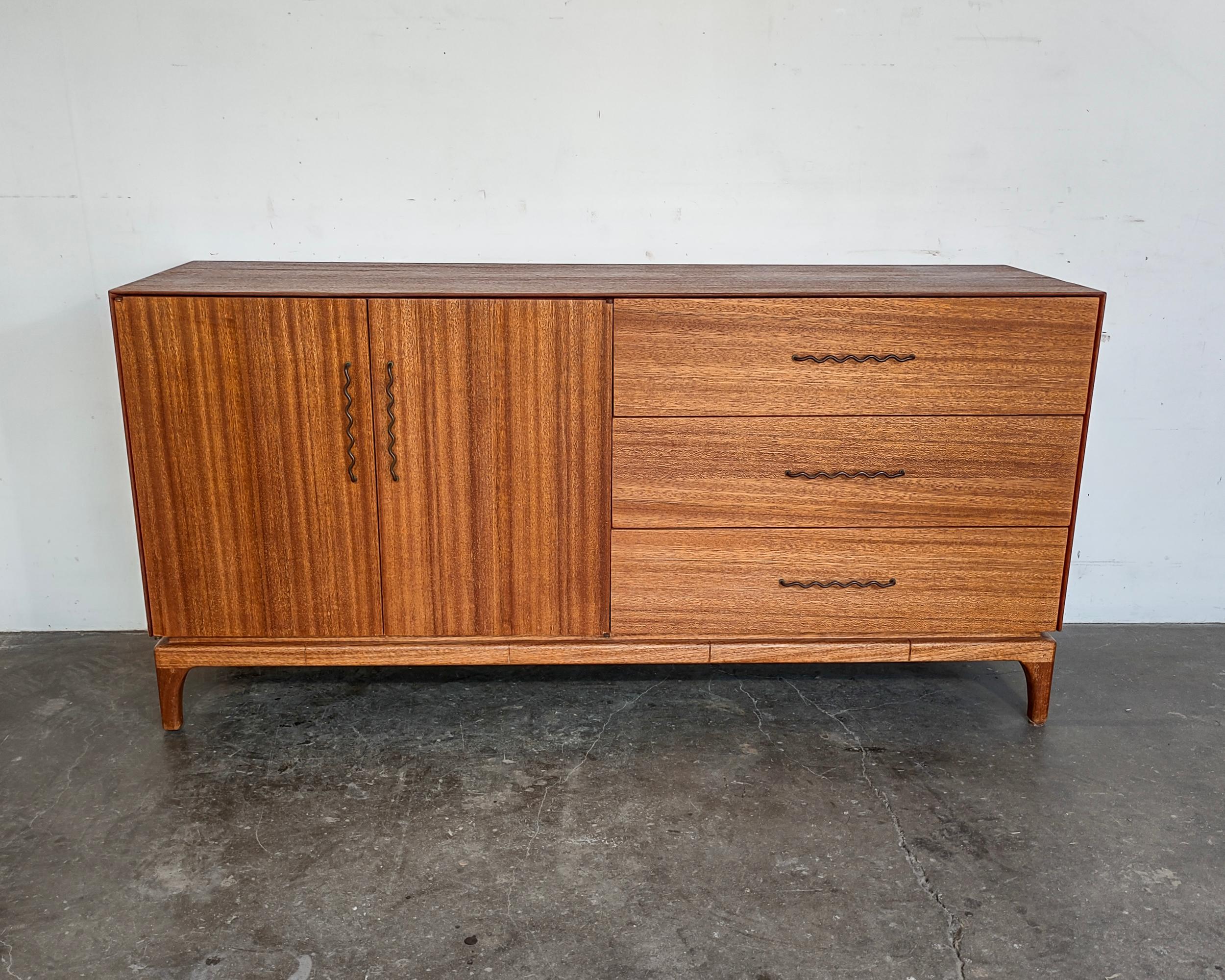 Completely restored 1960s mahogany wood credenza designed by John Keal for Brown Saltman. Stunning wood grain throughout complimented by bronze squiggle pulls. The piece features a cabinet on the left with an adjustable shelf and three drawers on