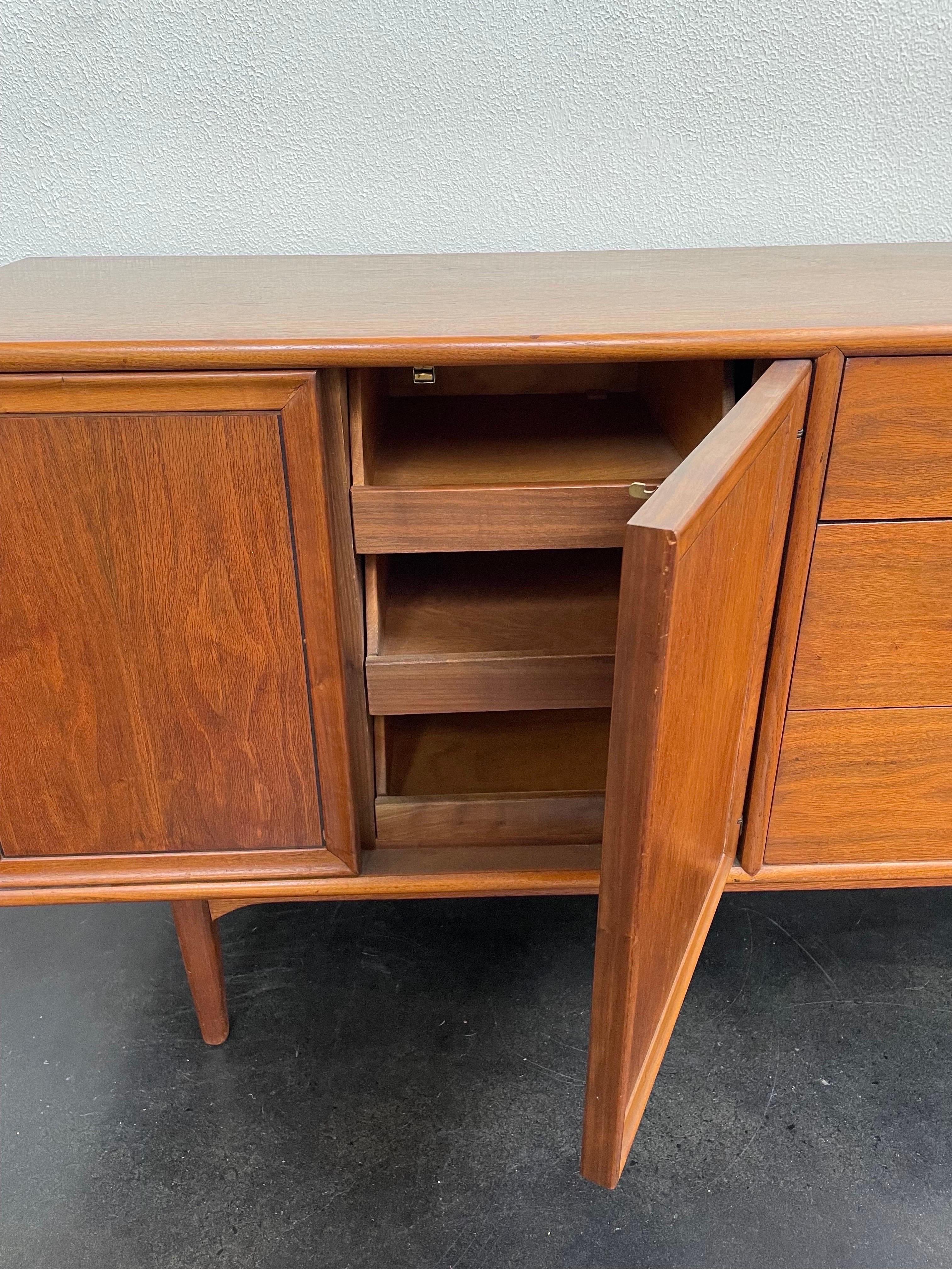 Vintage Mid-Century Modern credenza that could also be used as a dresser. This beautiful walnut wood credenza is designed by Kipp Stewart for Drexel and features four primary drawers with the original porcelain knobs.