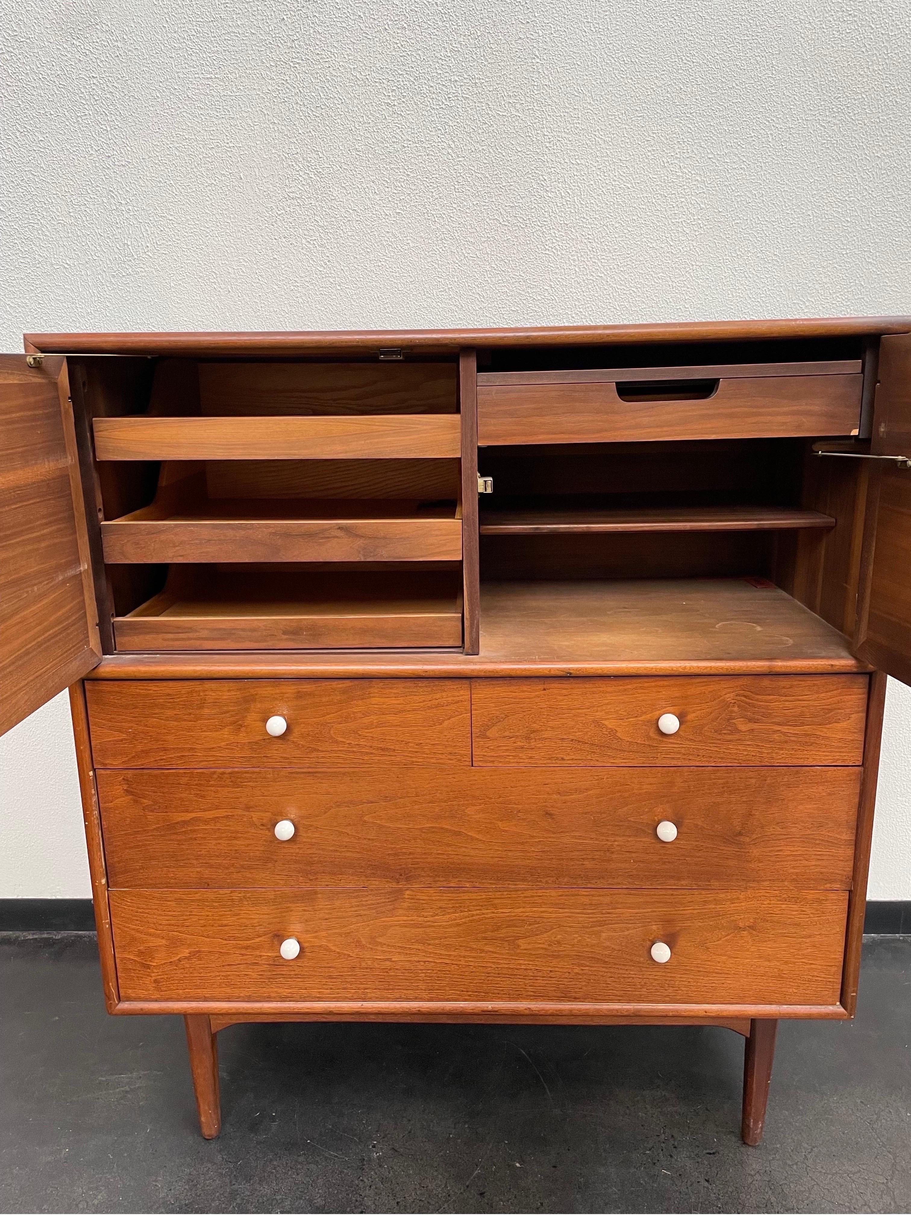 Vintage Mid-Century Modern highboy dresser with beautiful walnut wood. Designed by Kipp Stewart for Drexel and features drawers with original porcelain knobs. The upper half opens to reveal sliding drawers on left and a pull-out mirrored drawer with