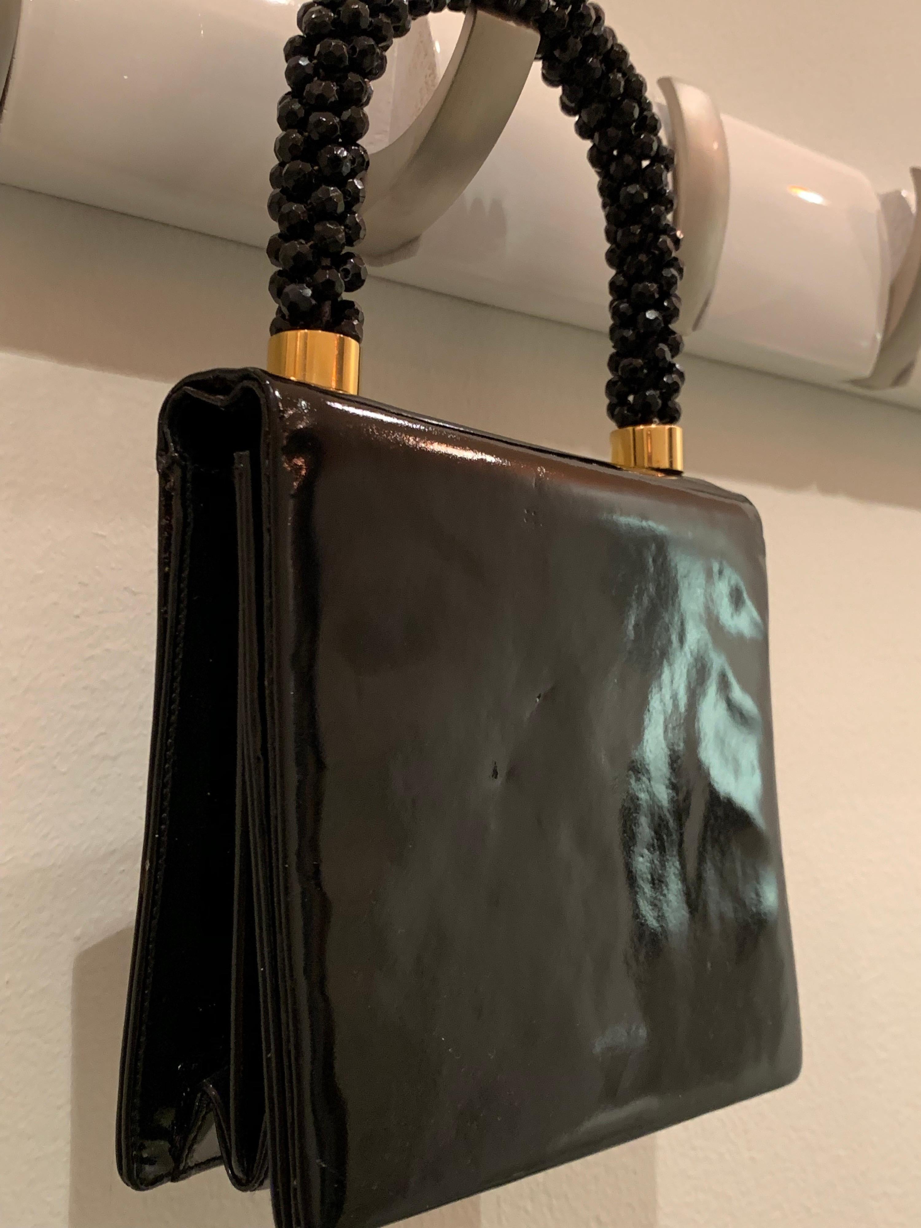 A smart 1960s Mod Koret handbag in genuine black patent leather. Handle is wrapped and covered entirely in black resin faceted beads. Snap flap closure.  inside pocket.   Bag measures 6