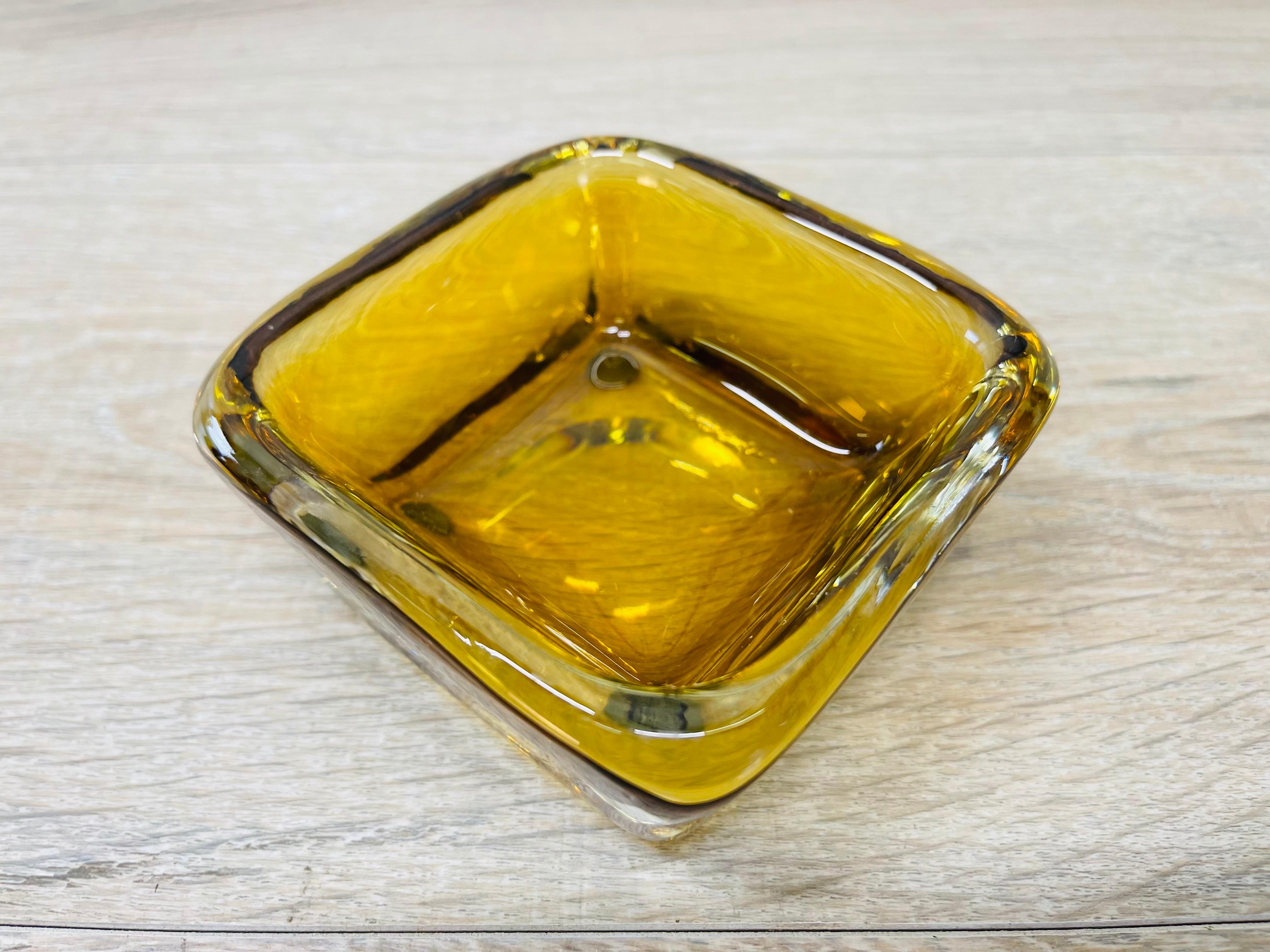 Vintage 1960s square glass ashtray by Kosta Boda. The ashtray is handblown in amber and clear glass. Marked underneath.