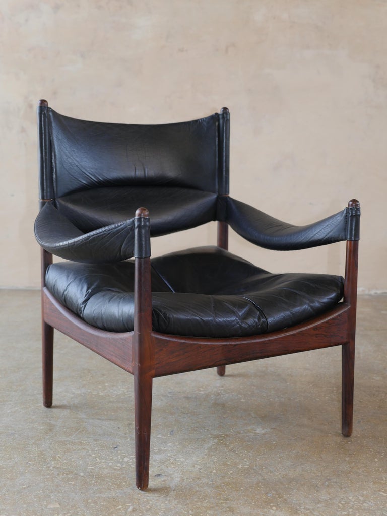 Mid-Century Modern Danish black leather lounge chair and ottoman with rosewood frames, model Modus by Kristian Vedel. This iconic chair is distinguishable by its leather sling arms and elegant rosewood frame, with arched curves and turned leg posts.