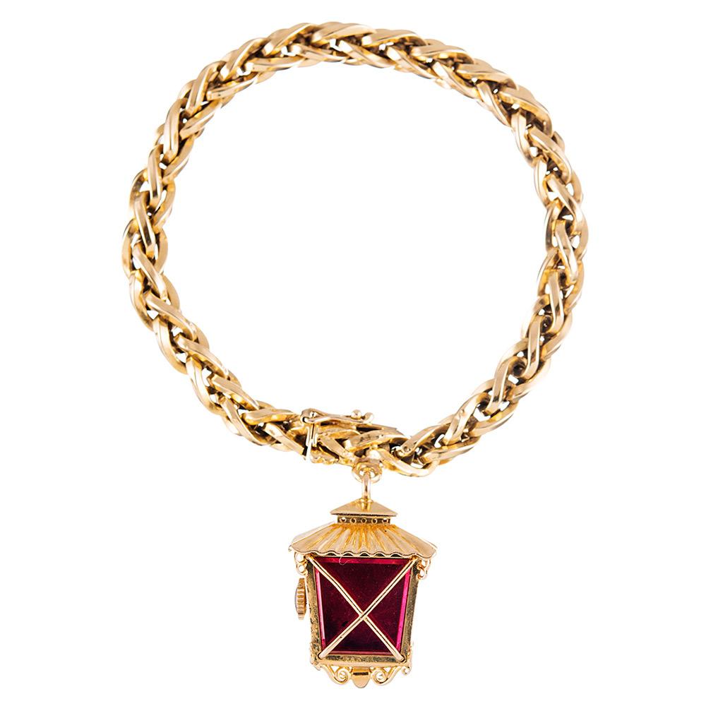 Vintage charm abounds... A truly unique twist on a classic charm bracelet, with an asymmetrical lantern-shaped manual wind watch suspended from a bracelet of 18 karat yellow gold links. Note the red enamel back and the textured honeycomb dial of the