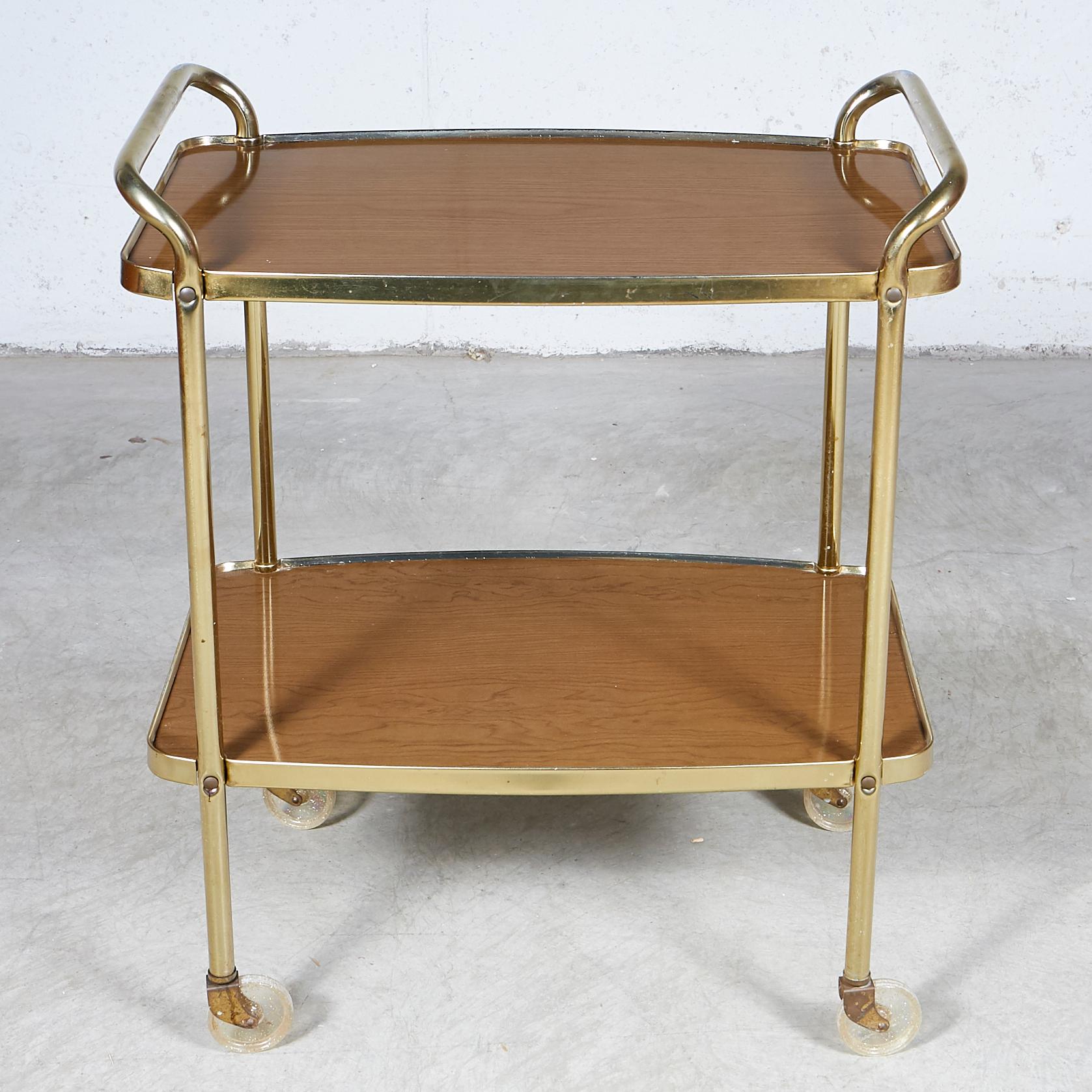 Vintage 1960s wood grain laminated two-shelf rolling serving cart by Cosco. The rolling cart has a gold metal accent. Light wear from use. Marked.