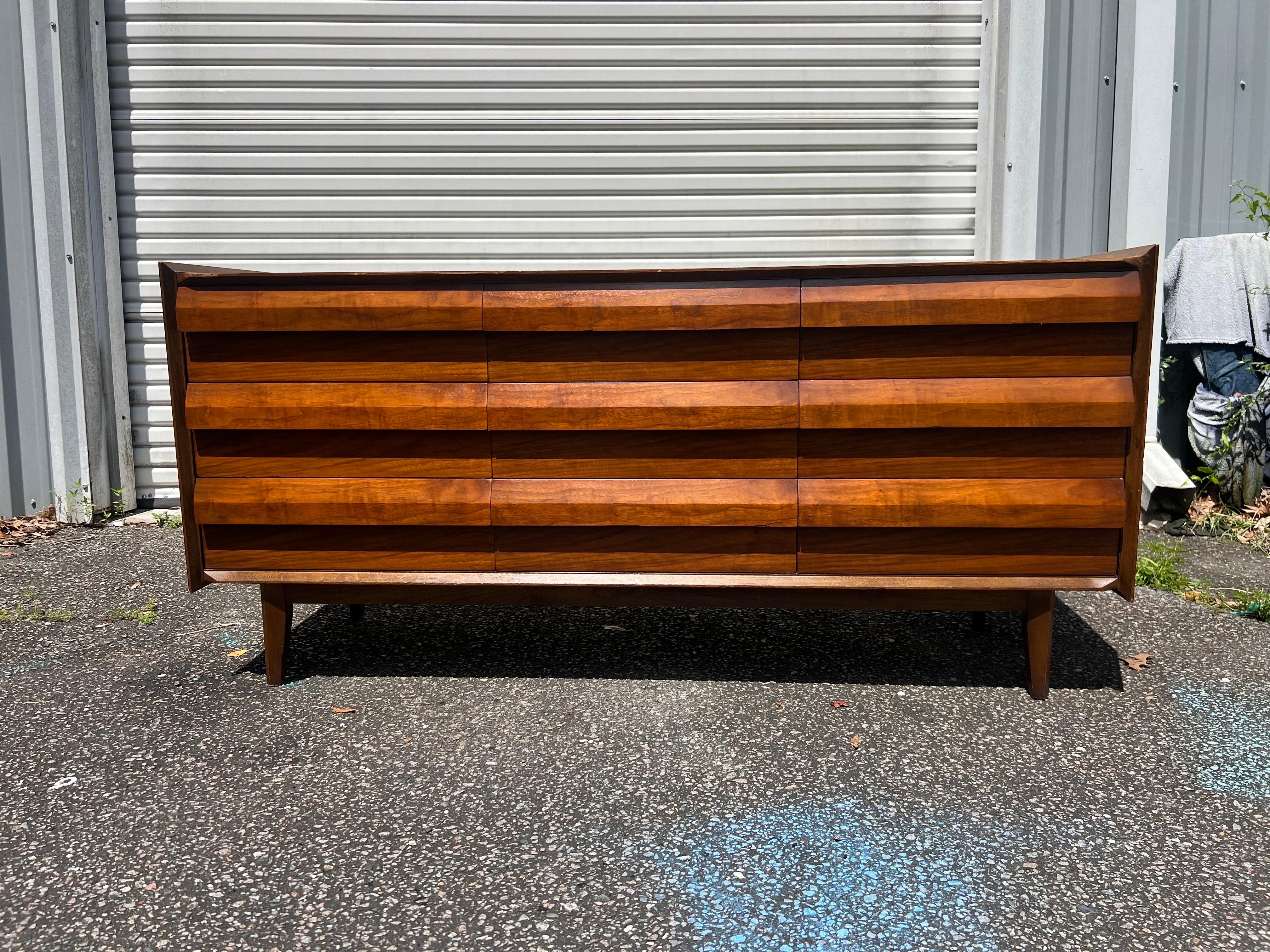 Arguably Lane's most coveted line. The First Addition Line is know for it's cascading angular design. This nine drawer dresser with ample storage is constructed from walnut. Angular beveled pulls for handles. Set on tapered legs. Circa 1960s.