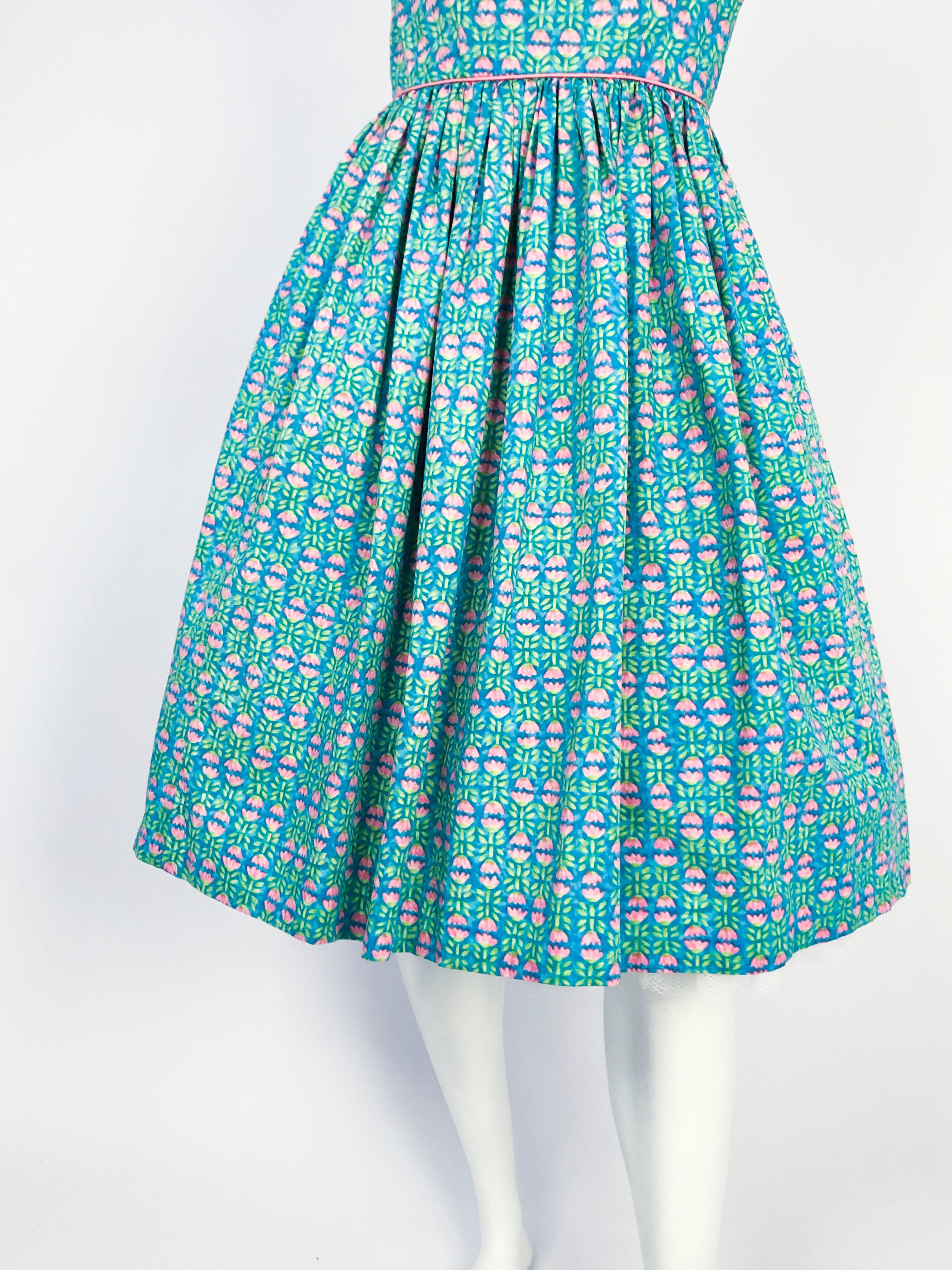 robe d'été imprimée Tulip de Lanz des années 1960. La couleur de base est un bleu aqua avec des tulipes rose layette et des feuilles vertes. La robe a un corsage ajusté avec une jupe complète (photographiée avec un jupon qui n'est pas inclus), des