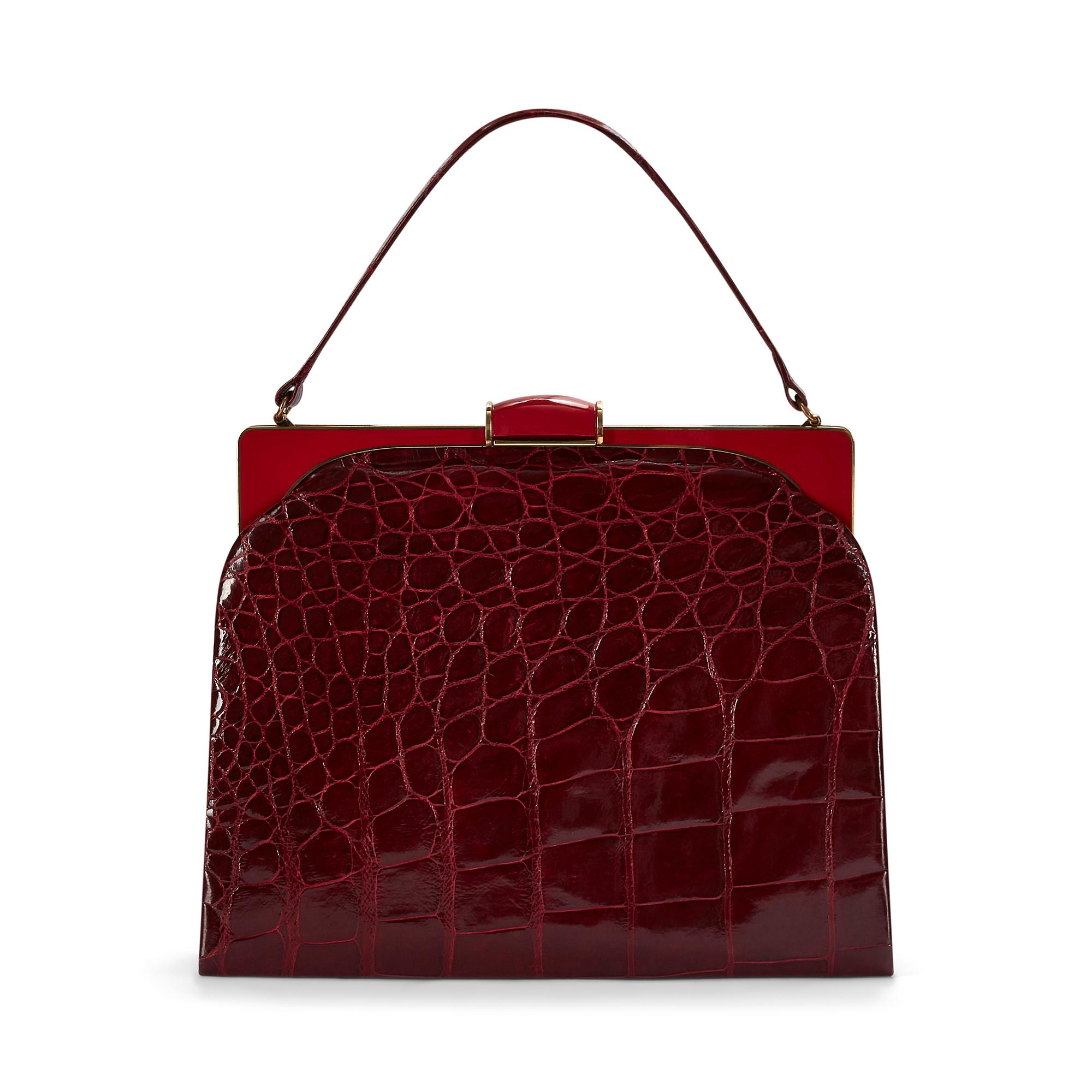 This elegant bag was made in the 1950s to early 1960s from fine dark red crocodile leather. The stiff boxy shape adds an easy formality, whilst the gold and red-tone enamel hardware and clasp make this a glamorous choice of bag for a daytime event.