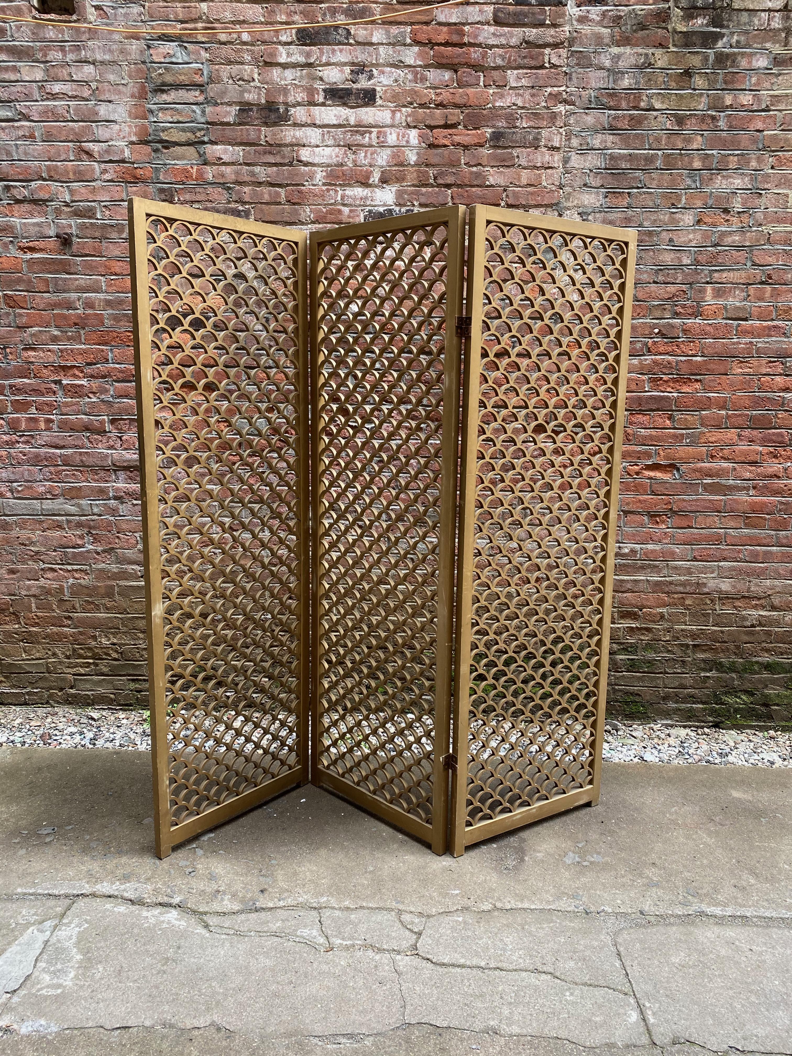 Large wood three-panel room divider/screen, circa 1960. Great architectural presence. Old gold paint. No visible breaks or damage to the screen. Some rusting to metal hinges. Minor wear, scuffs and dings to the wood and paint surface. Structurally