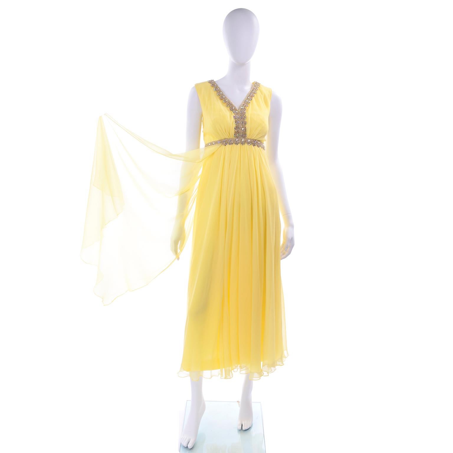 This is a beautiful yellow silk chiffon empire waist evening gown from the 1960's with pretty gold metallic trim and prong set rhinestones. The dress has flyaway panels in the front and closes with a metal back zipper and hook and eye. This fully