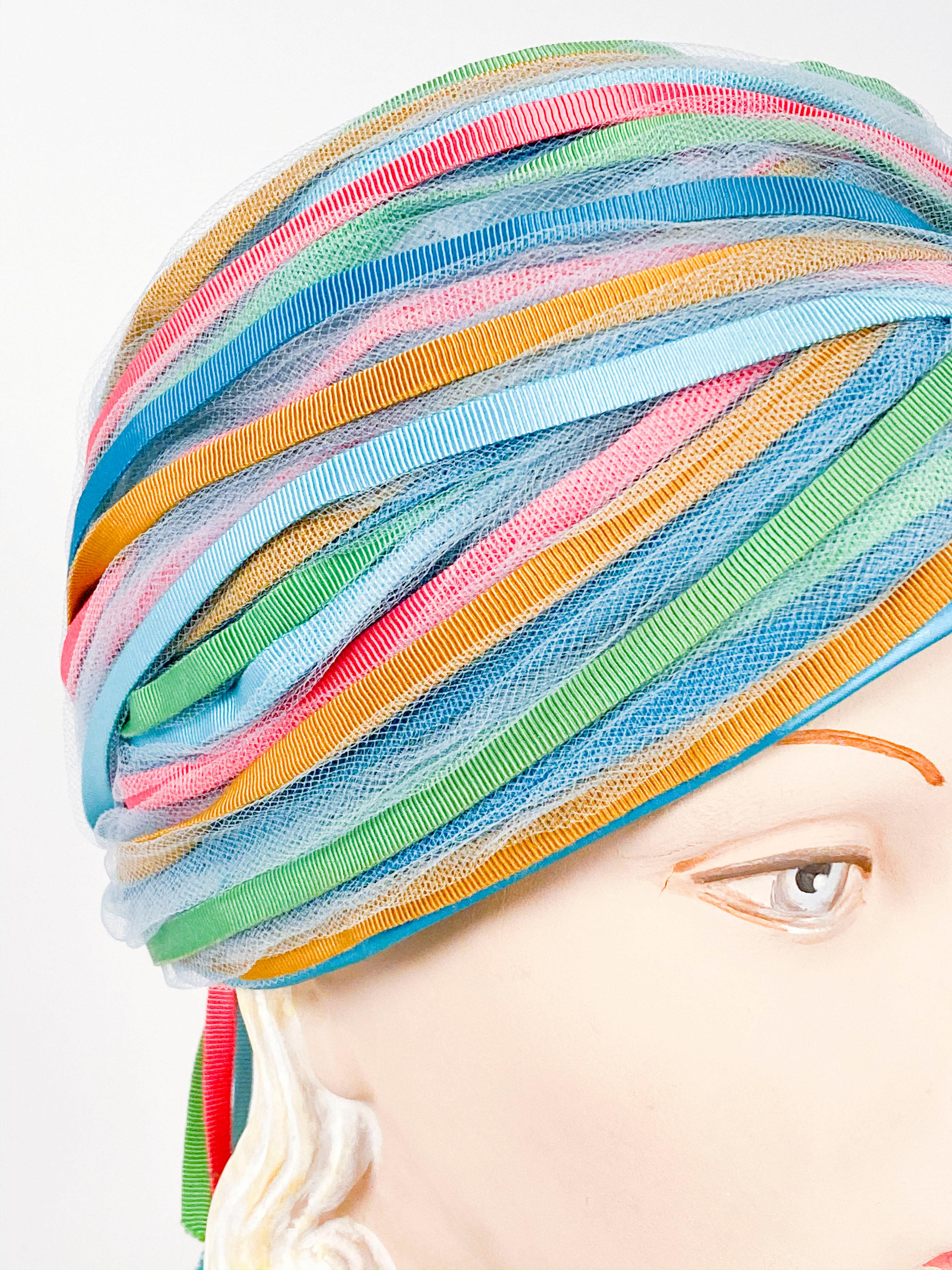 1960s light blue turban with gros-grain ribbon finishings in blue, light blue, lime, and hot pink gathered at the back with short tails. The base is made of a light blue netting and finished with satin.