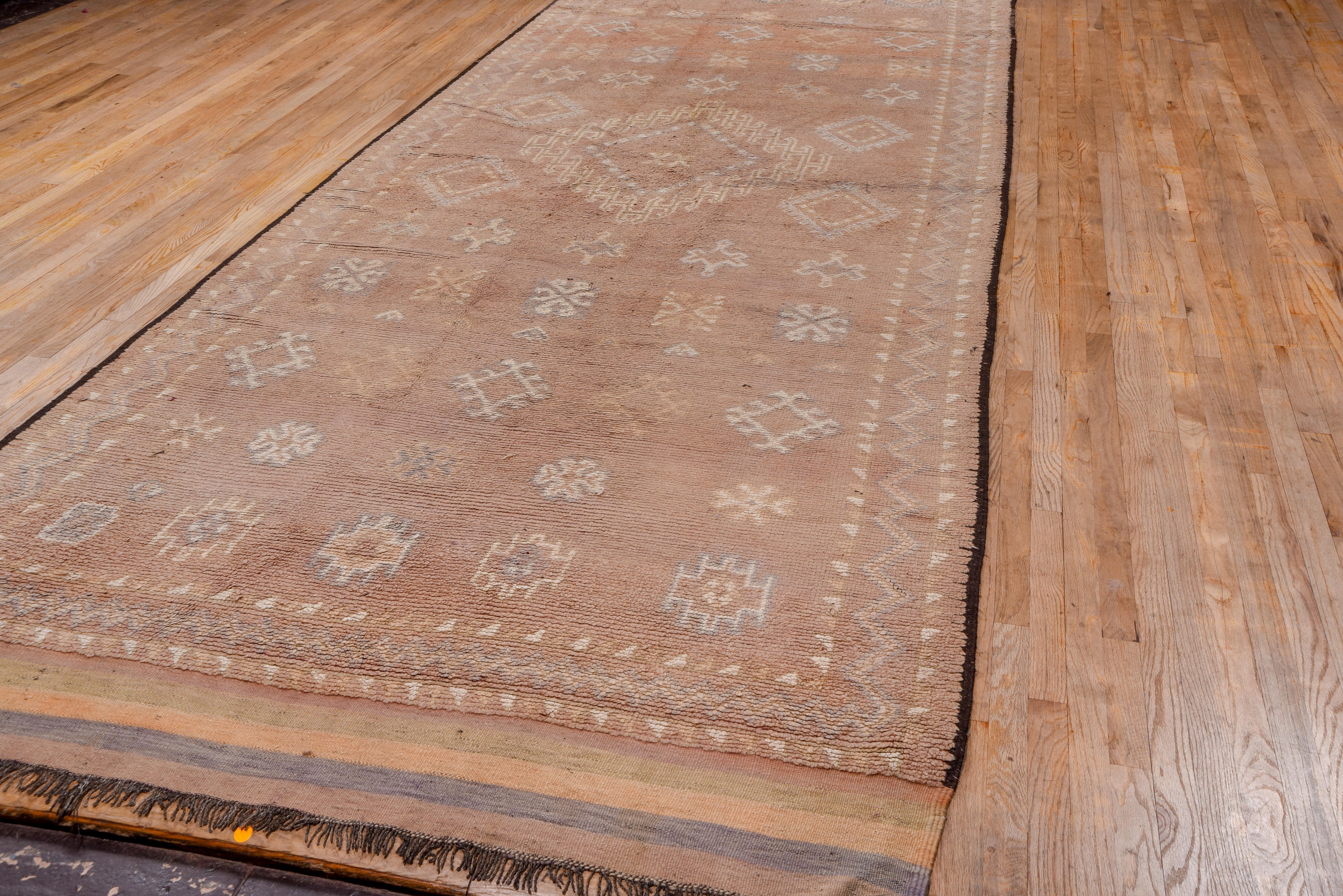 This high pile, coarsely woven tribal carpet displays a very soft coral field presenting a large central diamond medallion with a connected and hooked H surround, with five rows both above and below of five stars each. Ivory details. Narrow coral