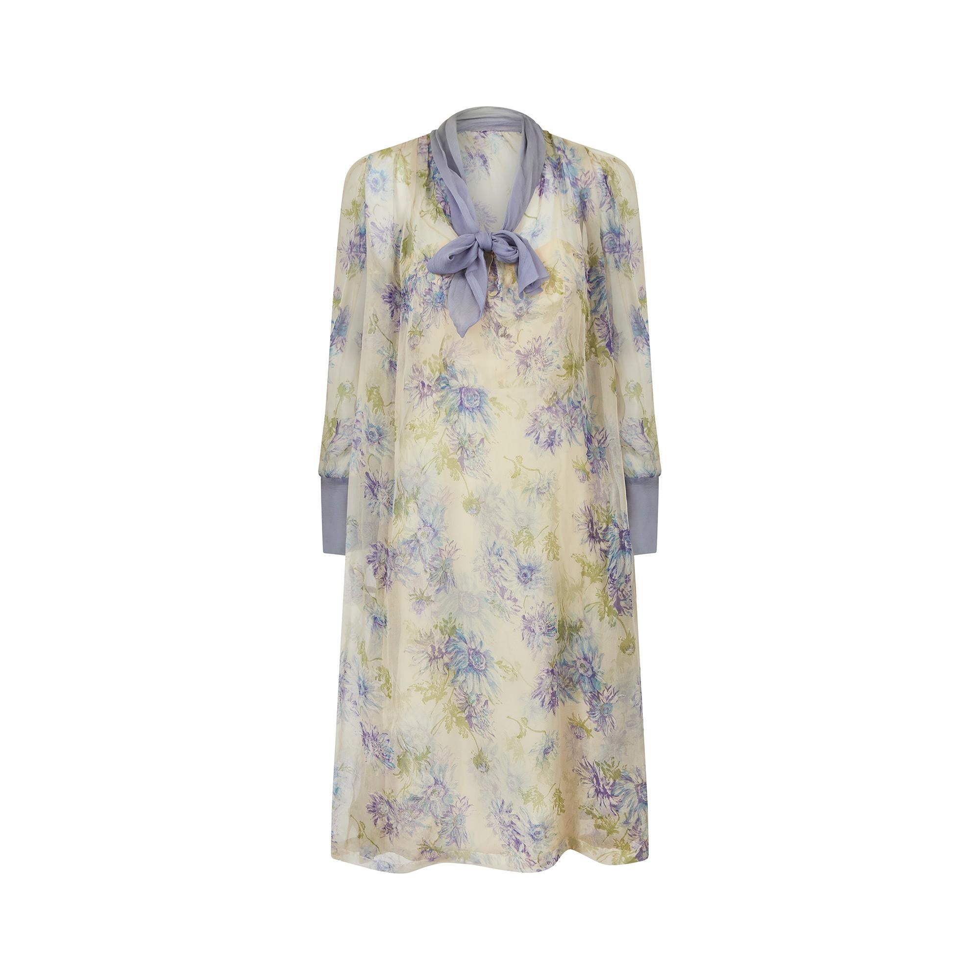 This is a beautifully feminine, early 1960s silk floral print dress ensemble and perfect for more formal occasions. The outer layer is crafted in a loose, shift like shape complete with attached lilac tie scarf and cuffs.  It slips on over the head