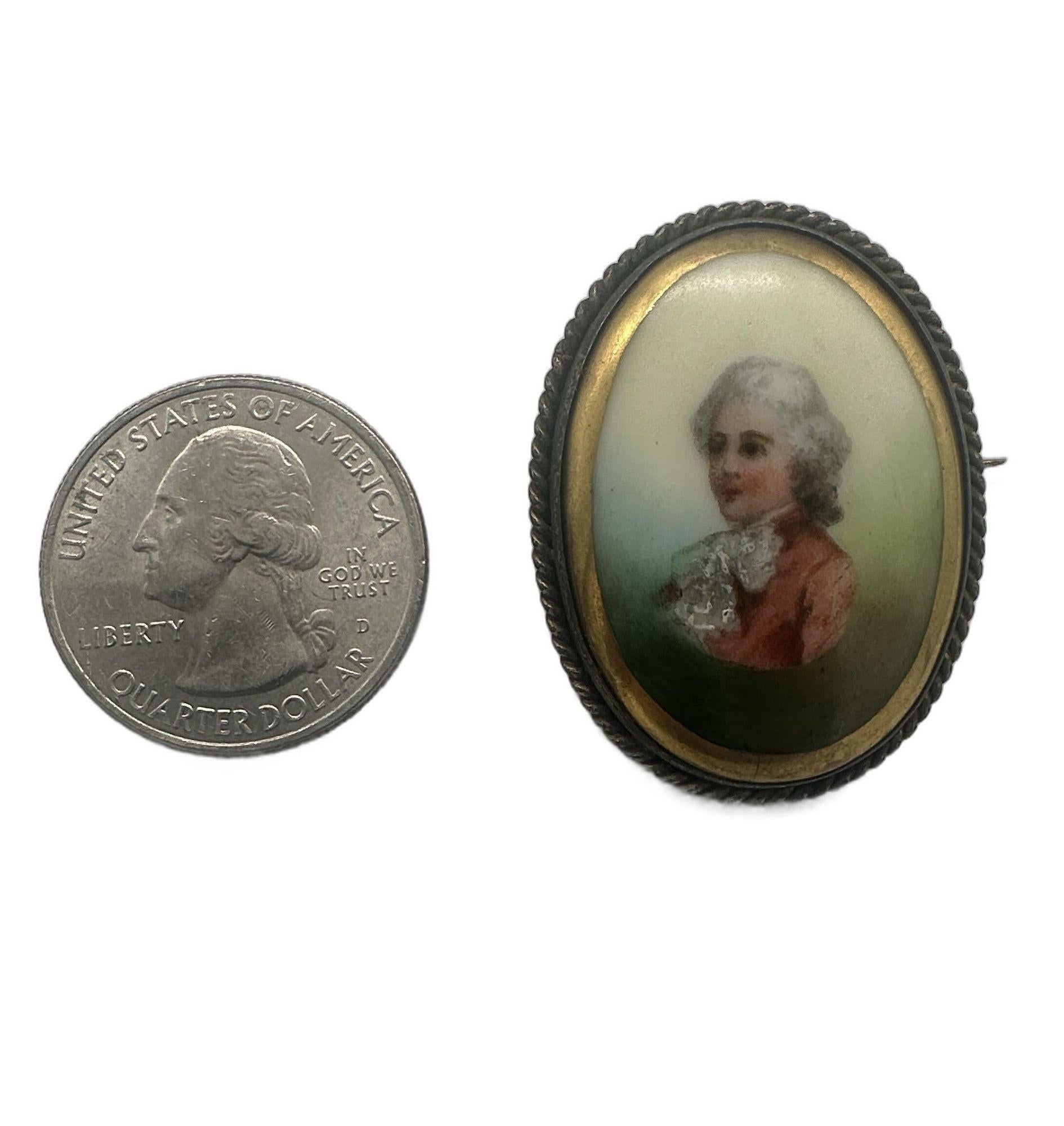 La descrizione si riferisce a una piccola spilla con un ritratto dipinto a mano di un nobile. Il nobile è raffigurato con un abito rosa, uno stile popolare durante il periodo Rococò, noto per la sua moda stravagante e decorata. Inoltre, indossa una