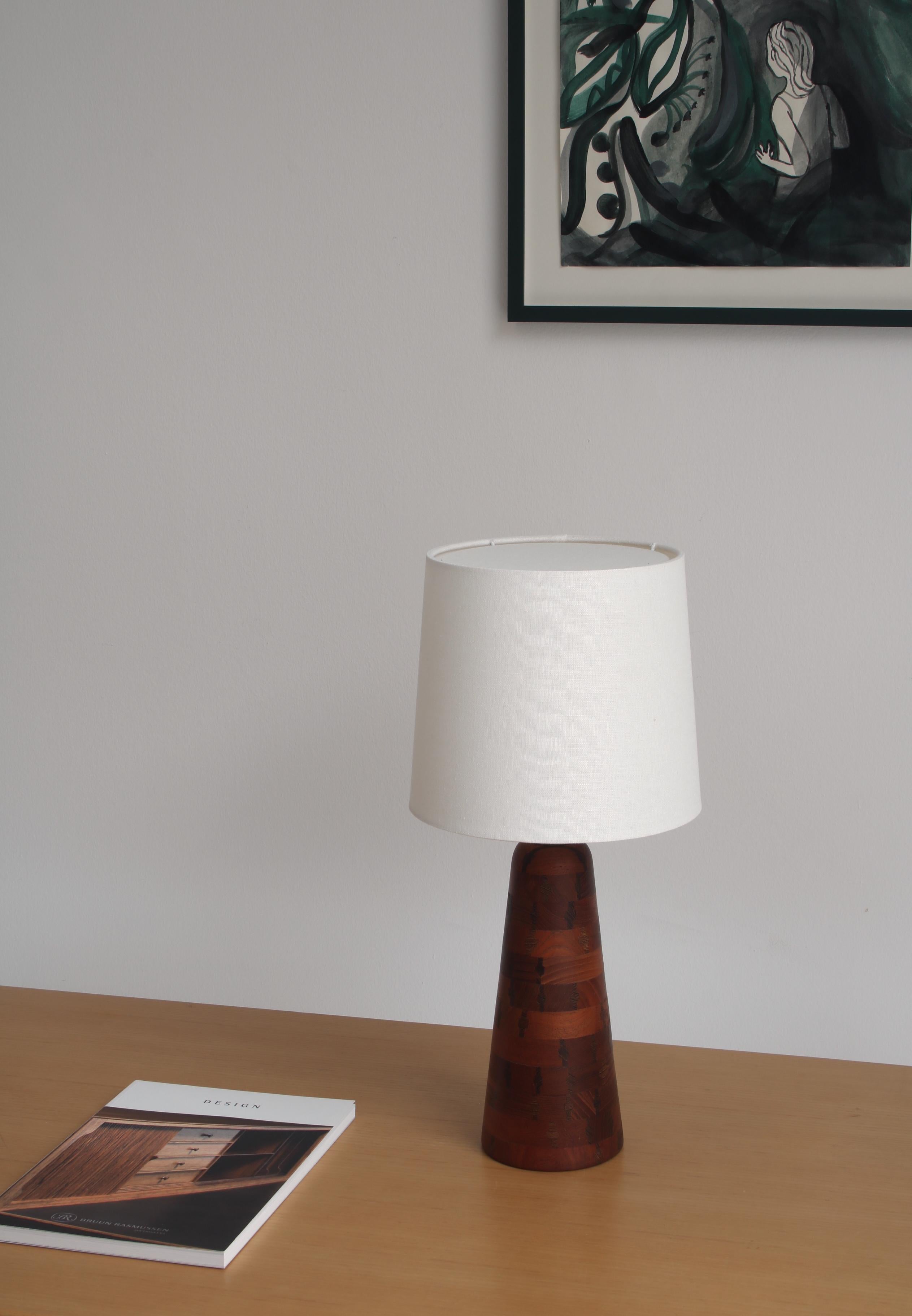 Decorative table lamp in teakwood and brass from the 1960s attributed to Danish designer Lisbeth Brams. The Lamp base is made of single pieces of teakwood connected with visible joints in dark wenge. The lamp has been mounted with a new flax linen