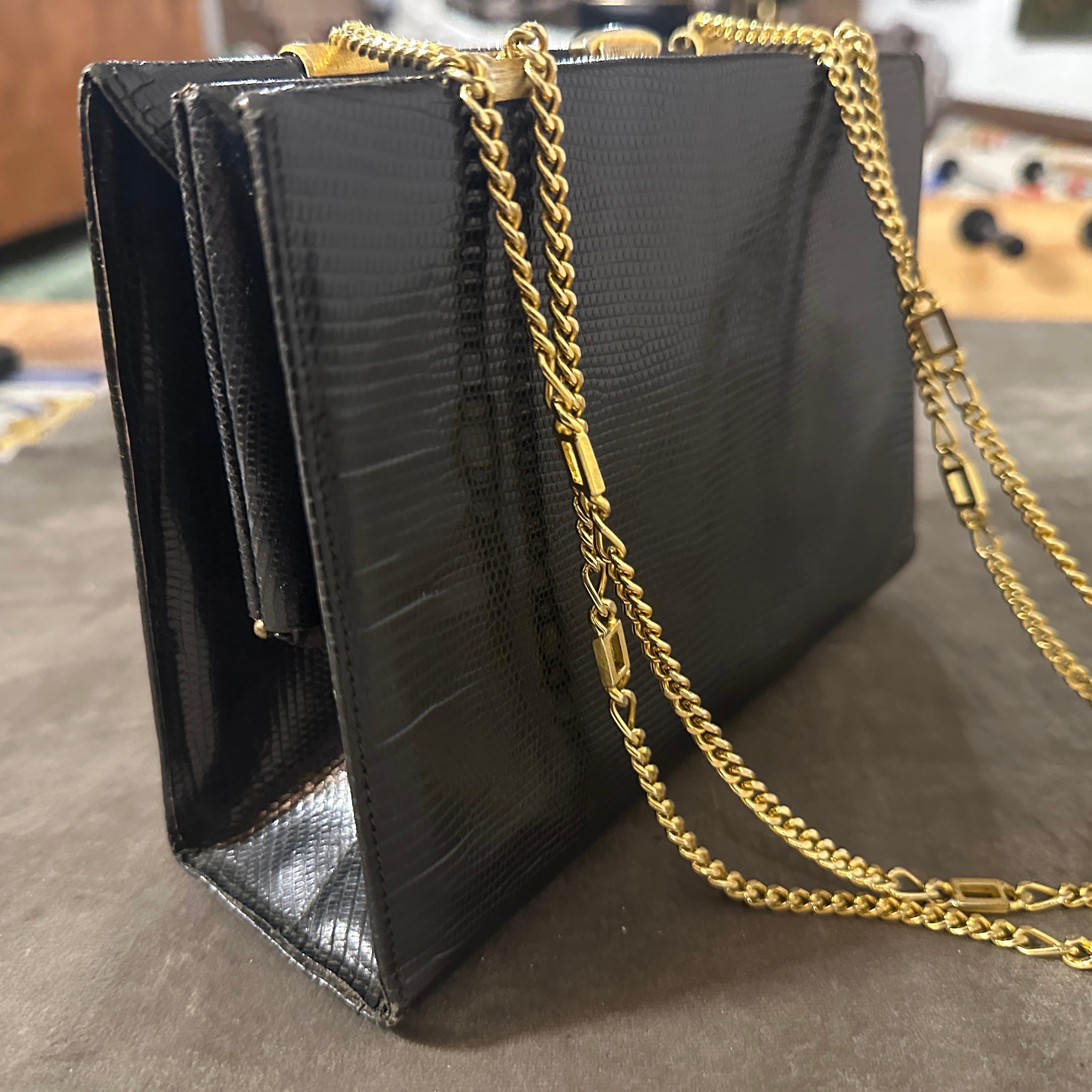 This vintage handbag from the 1960s is a sophisticated example of mid-century elegance. Crafted from glossy black leather, the bag features a refined texture that enhances its timeless appeal. Its structured rectangular shape is both practical and