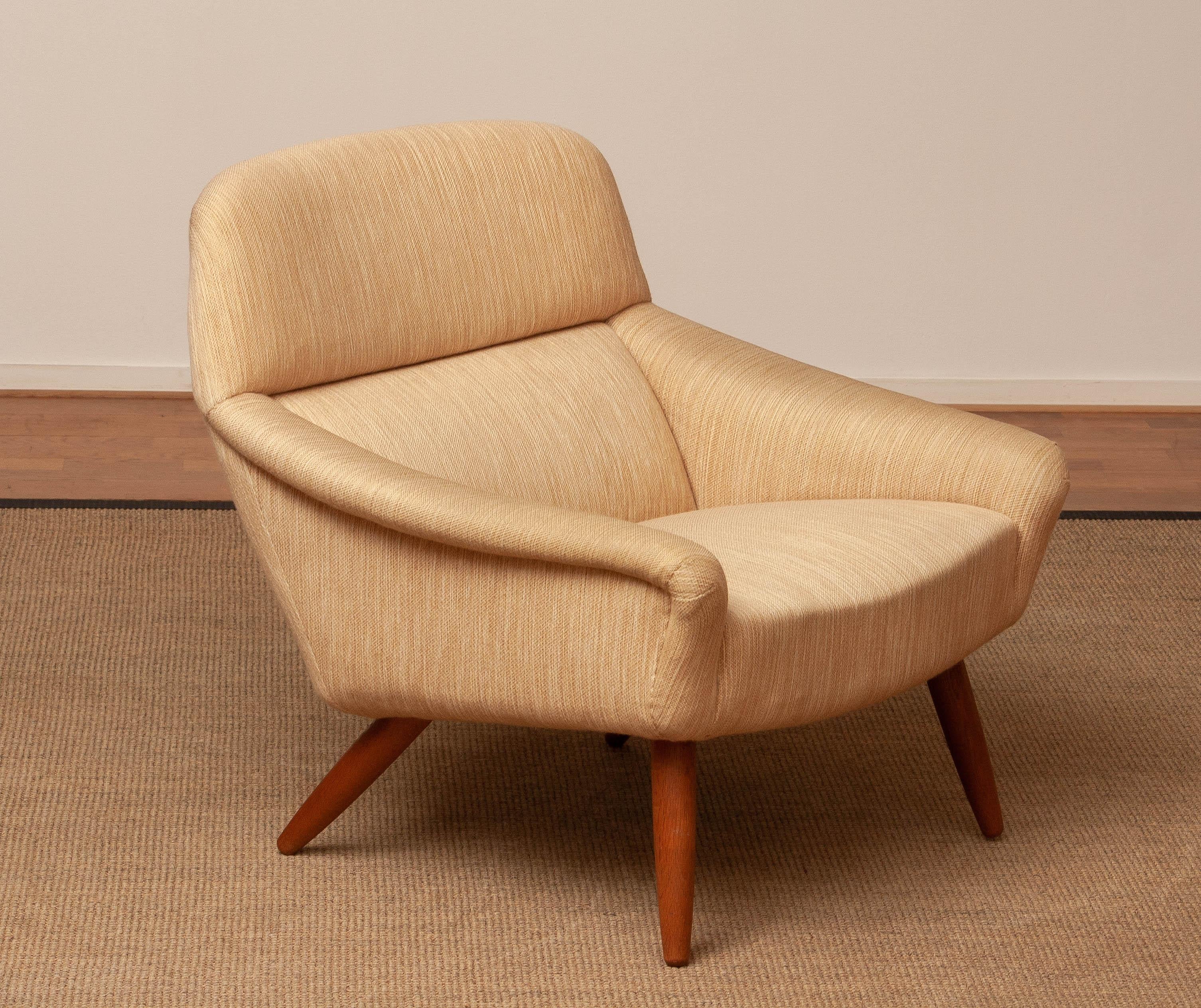 Este elegante sillón de los años 60 de Leif Hansen, fabricado por Kronen Denmark, ejemplifica el diseño danés atemporal. La silla tiene un armazón bellamente esculpido con patas de roble macizo, que ofrece estabilidad y calidez natural. Tapizado en