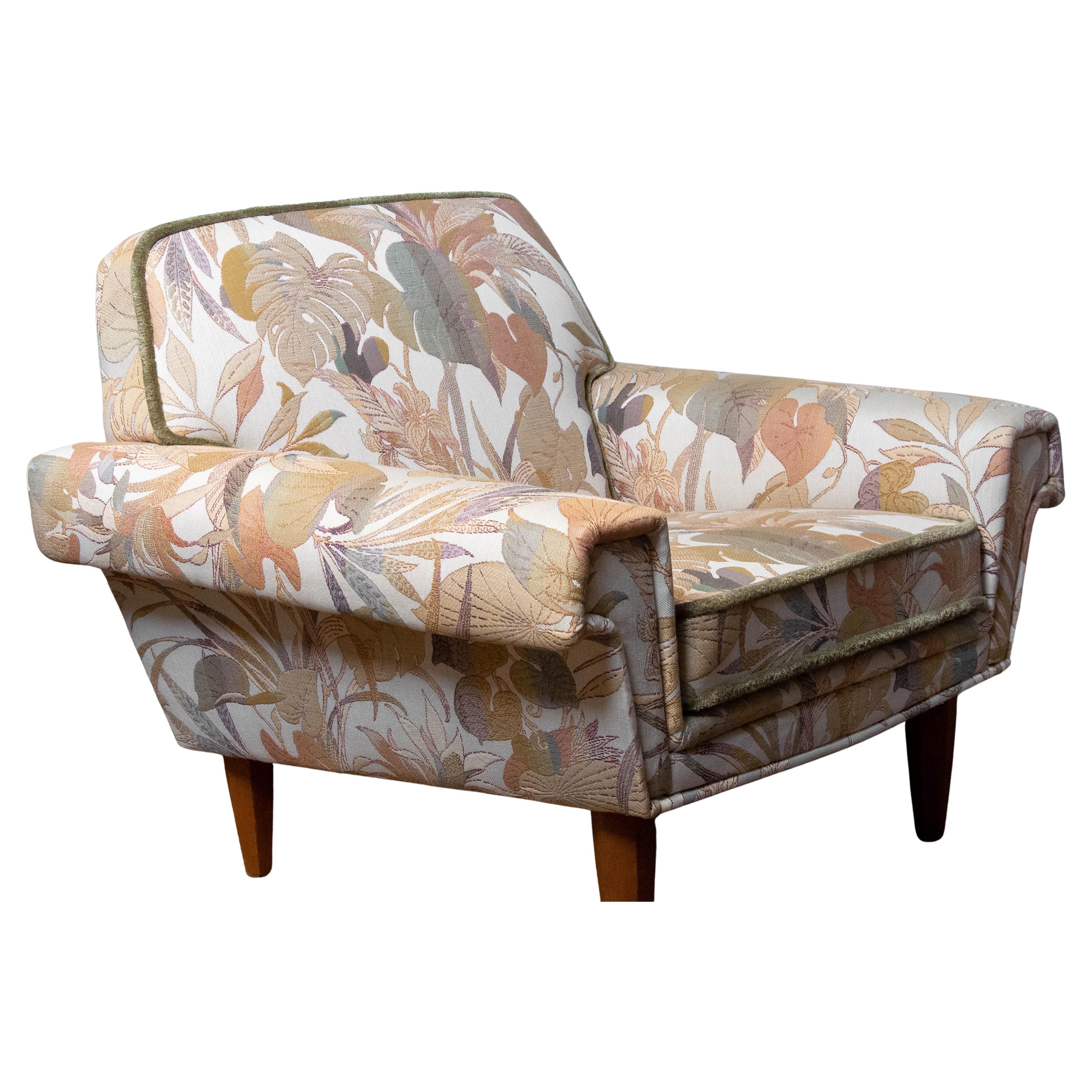 Una encantadora tumbona de los años 60 fabricada por Trensums en Suecia, tapizada en una tela jacquard de rica textura. El estampado presenta suaves tonos terrosos y un elegante motivo botánico, que confieren a la silla una presencia cálida y