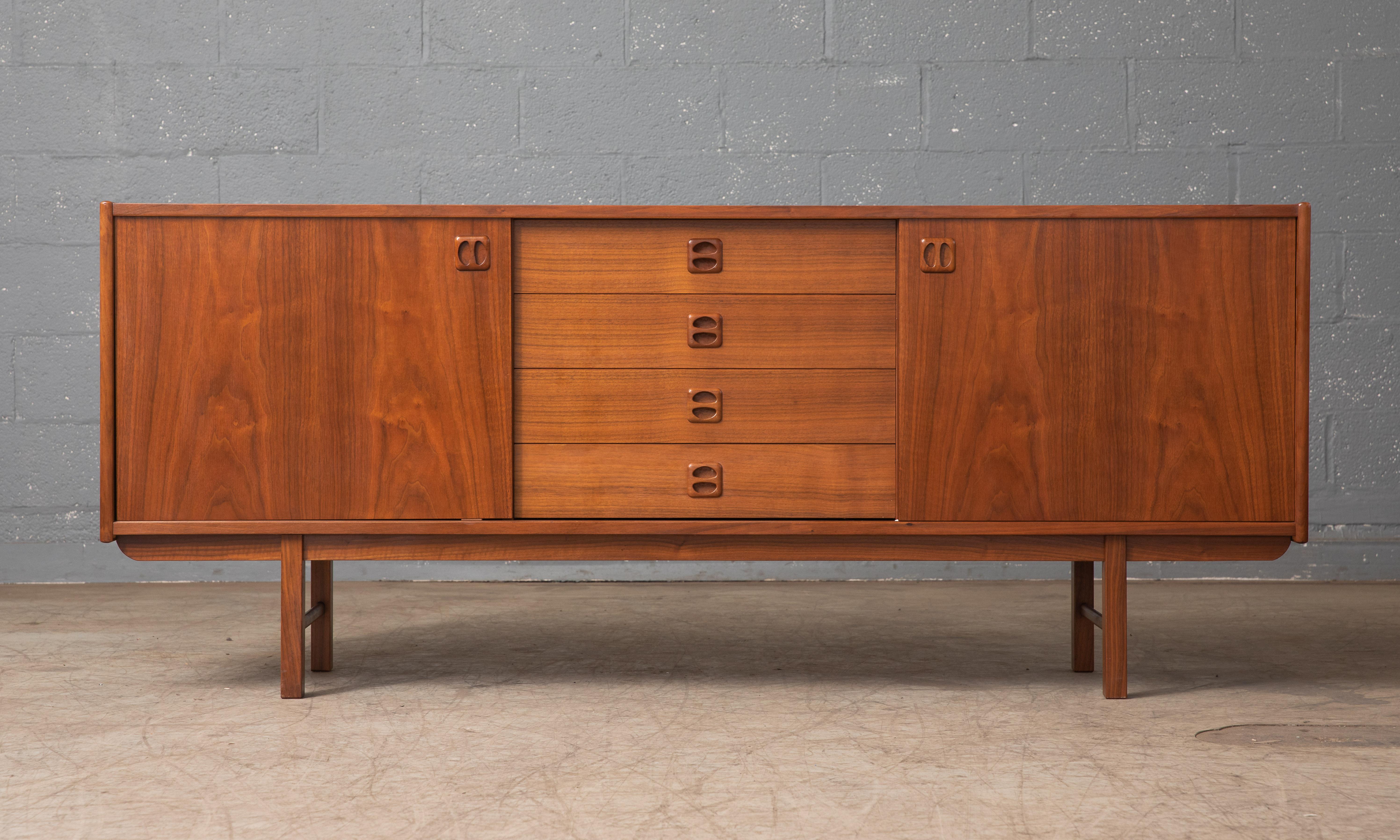 Beautiful Danish 1960s low sideboard in teak in the style of Kai Kristiansen. Nice center drawer section flanked by compartments with adjustable shelves behind nice bookmatched sliding doors with carved pulls. Nice base in solid teak. Very elegant