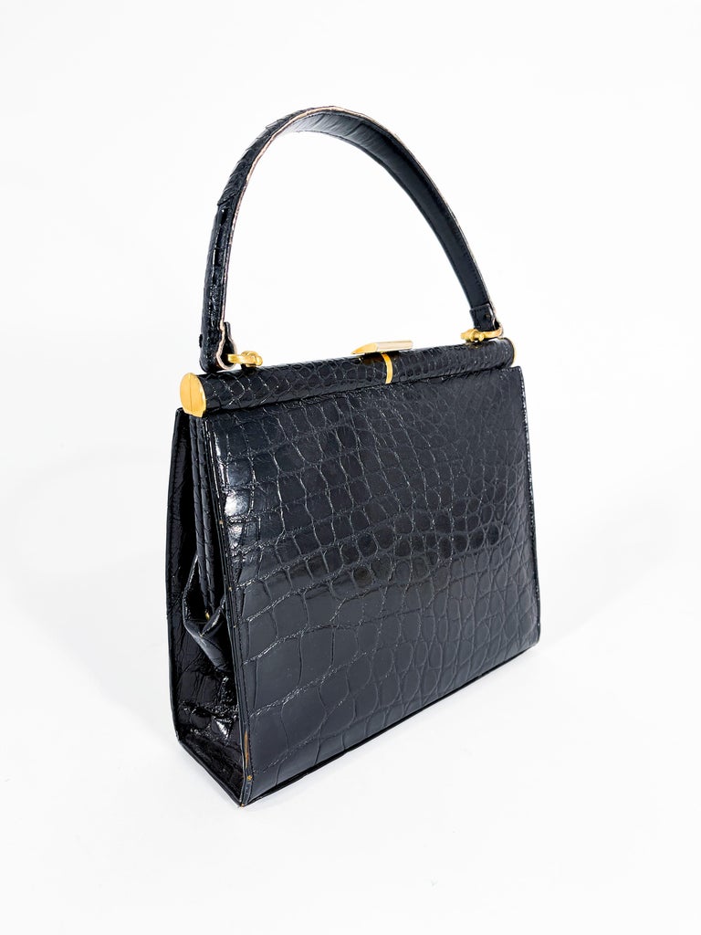 1960s Lucille de Paris Black alligator top handle handbag with a bras frame and hardware. The interior has a black leather lininging with three pockets and one additional zippered pocket. The bottom of the bag features four brass feet to further