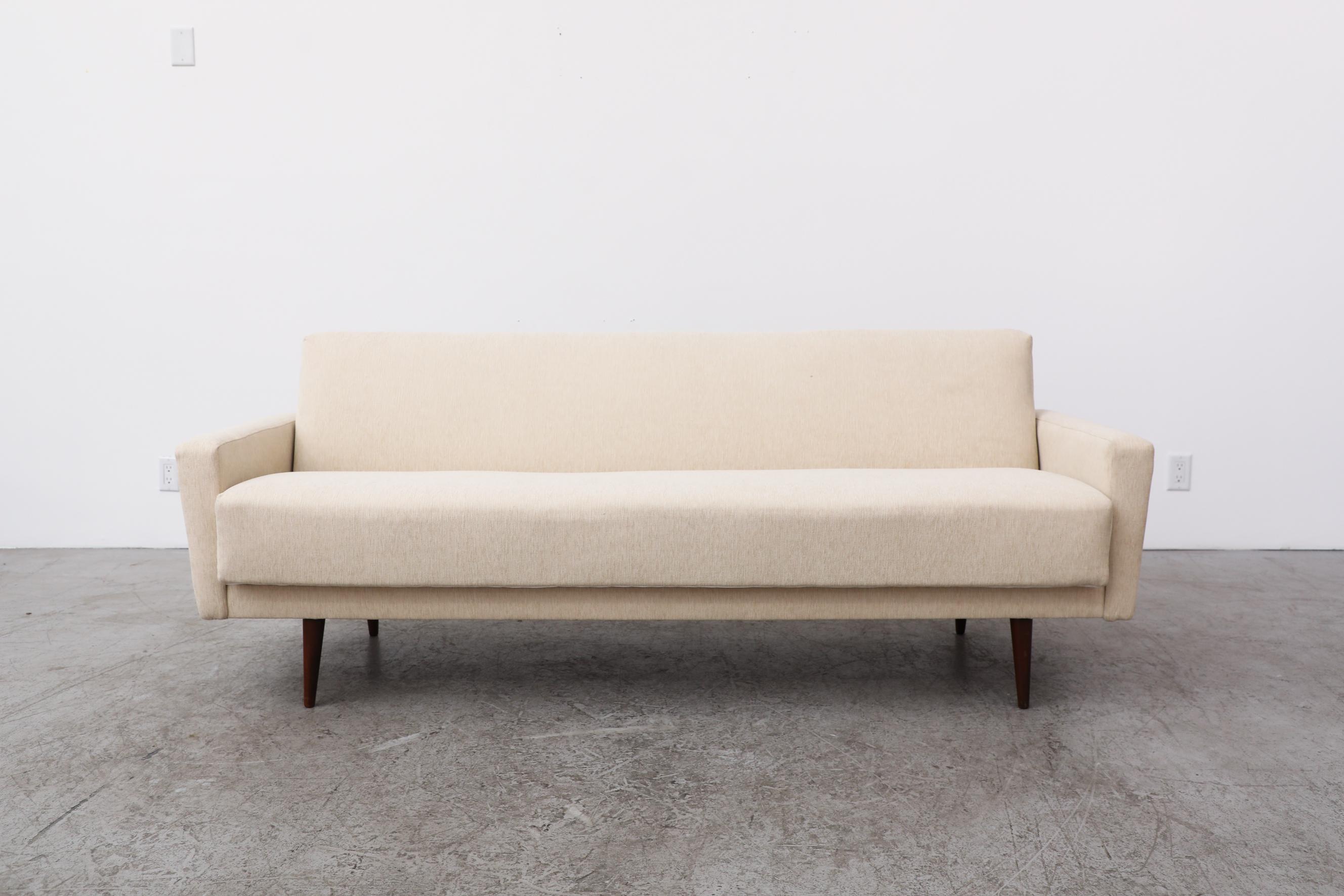 Mid-Century, stylishly boxy, 3 seater sleeper sofa with tapered teak legs and newly upholstered cream fabric. The back folds down to convert from sofa into a bed. Bed measures 78