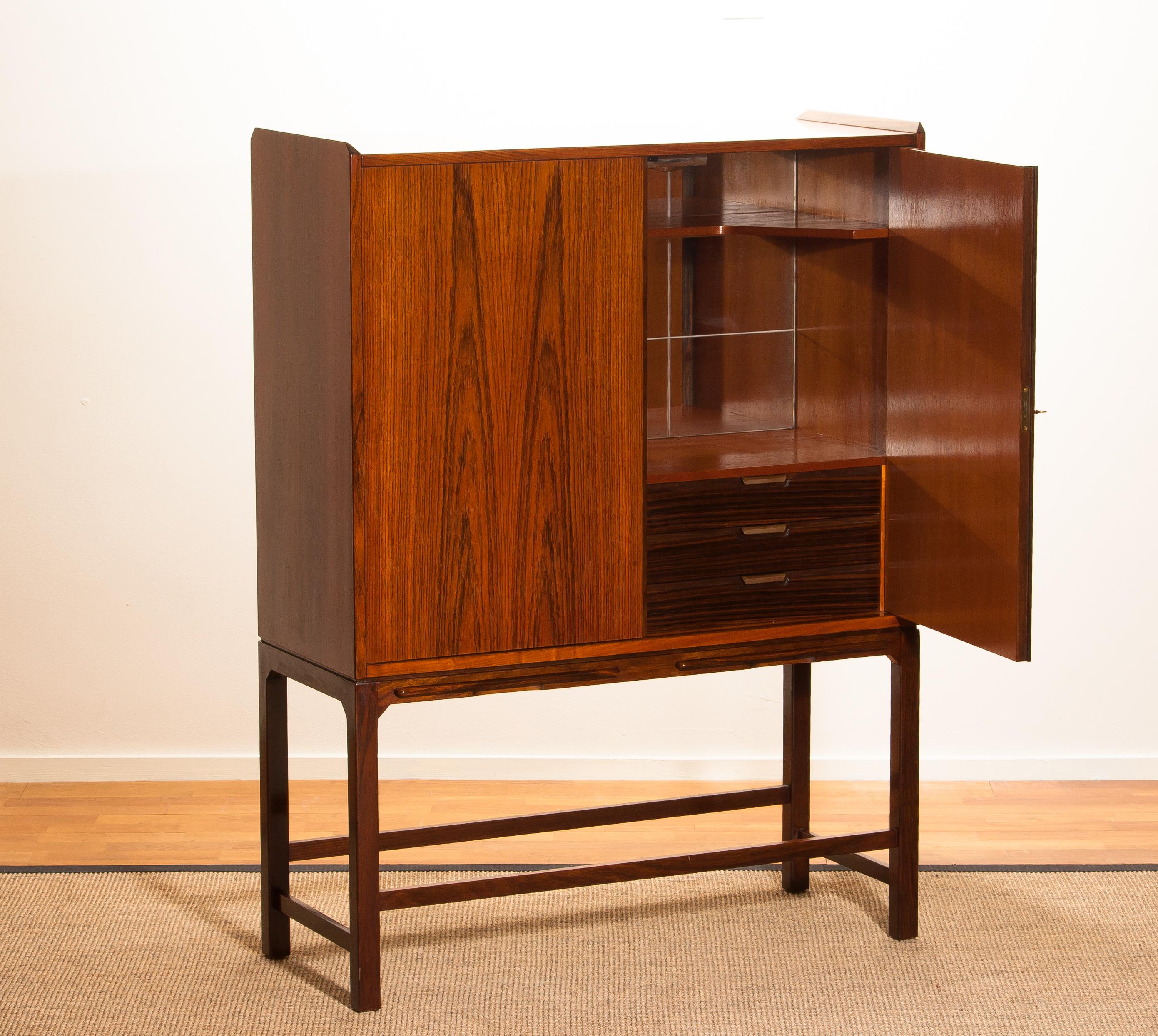 Exceptional beautiful and in perfect condition dry bar/cocktail cabinet of mahogany on a skinny walnut stand. In the walnut, stand are two extendable shelves.
Inside the cabinet is made of teak. The three drawers are in walnut. The drawers are