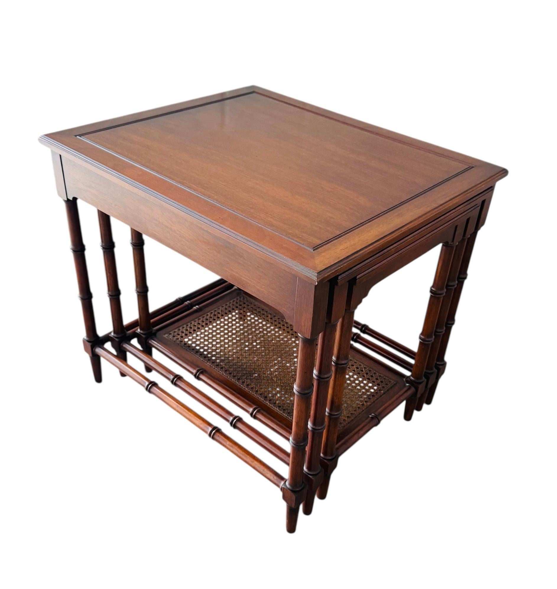 These are vintage mahogany nesting tables designed with elegant faux bamboo legs and a classic rectangular profile. The set includes a larger main table with two smaller tables that slide neatly underneath. Each table features a rich mahogany finish