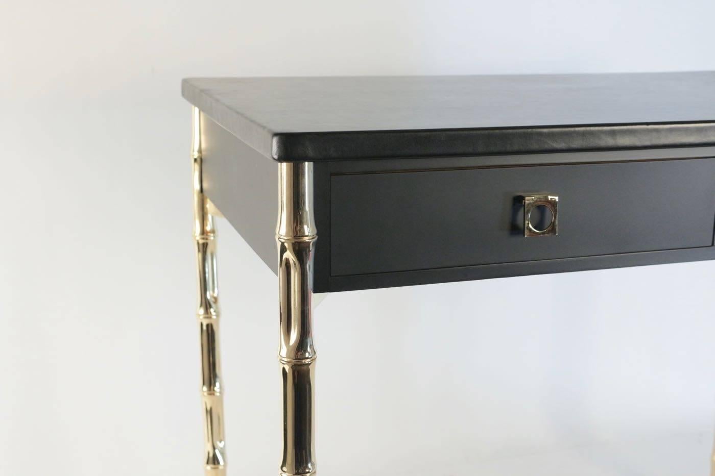 Maison Jansen desk from the 60's with Guy Lefèvre brass handles.

The top of the desk is in black leather, the two front drawers are adorned with Guy Lefèvre gilded brass handles.
It rests on four bamboo feet with crossed braces in gilded brass.
  