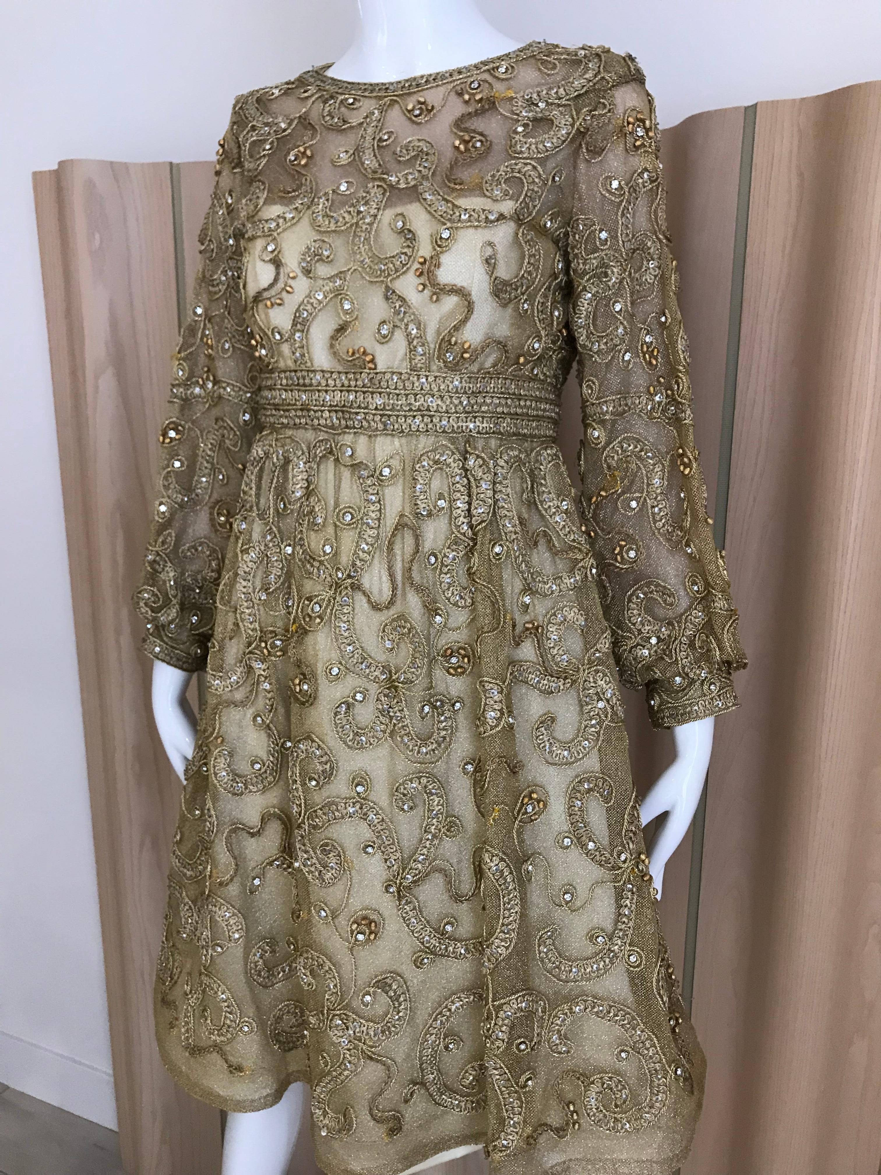 Vintage Malcolm Starr gold net overlay dress embellished with gold metallic braided ribbon and rhinestones. 
Dress has Scoop neck, fitted waist, poet sleeves with gathered cuff, sequins and rhinestones . Dress is lined, zipper up the back, covered