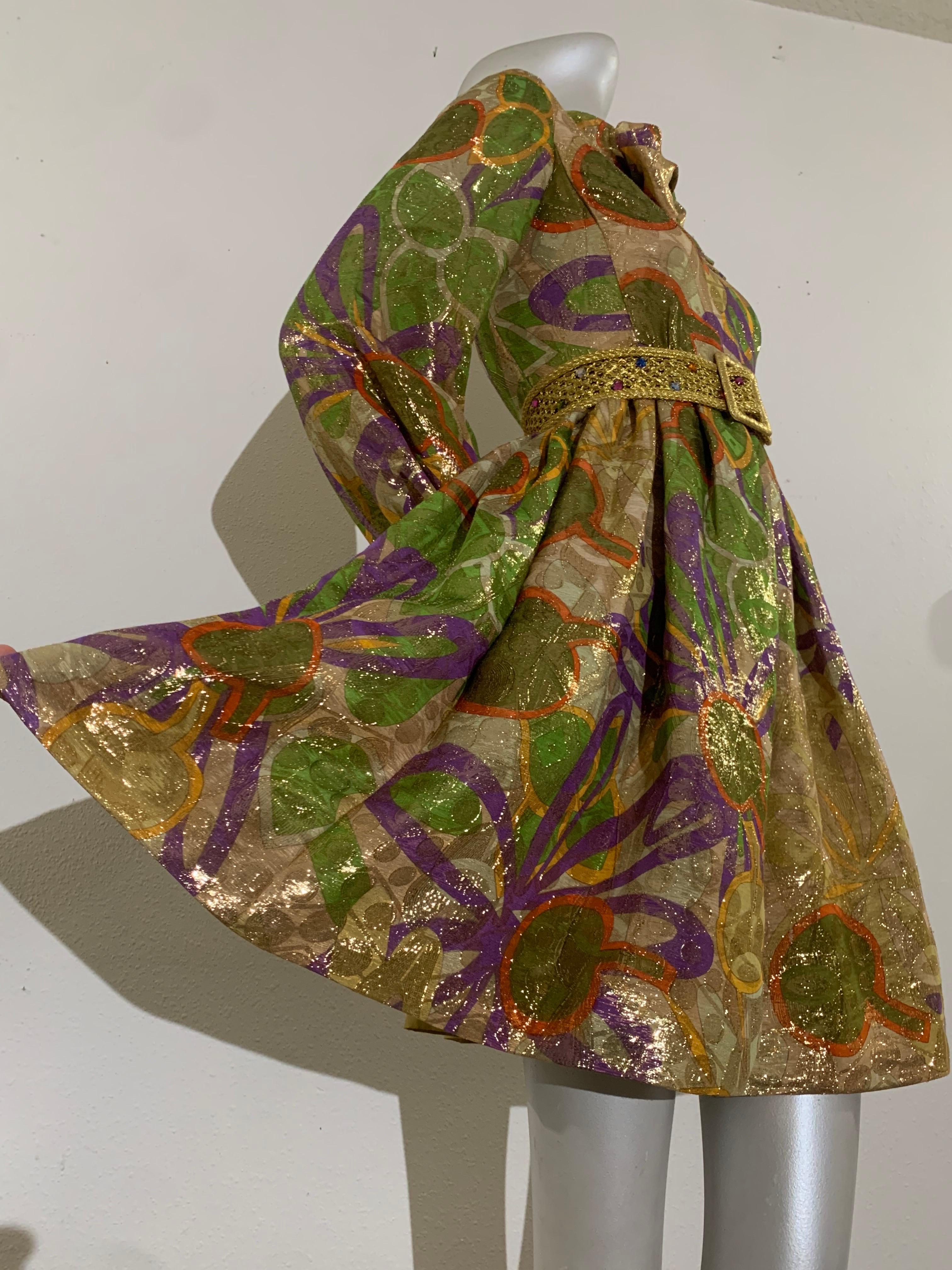 Minivestido de cóctel con estampado floral de los años 60 de Malcolm Starr:  Un extravagante y coqueto brocado cojo dorado con flores abstractas verdes y moradas. Cintura y corpiño entallados con minicamiseta completa y mangas globo. Bolsillos con
