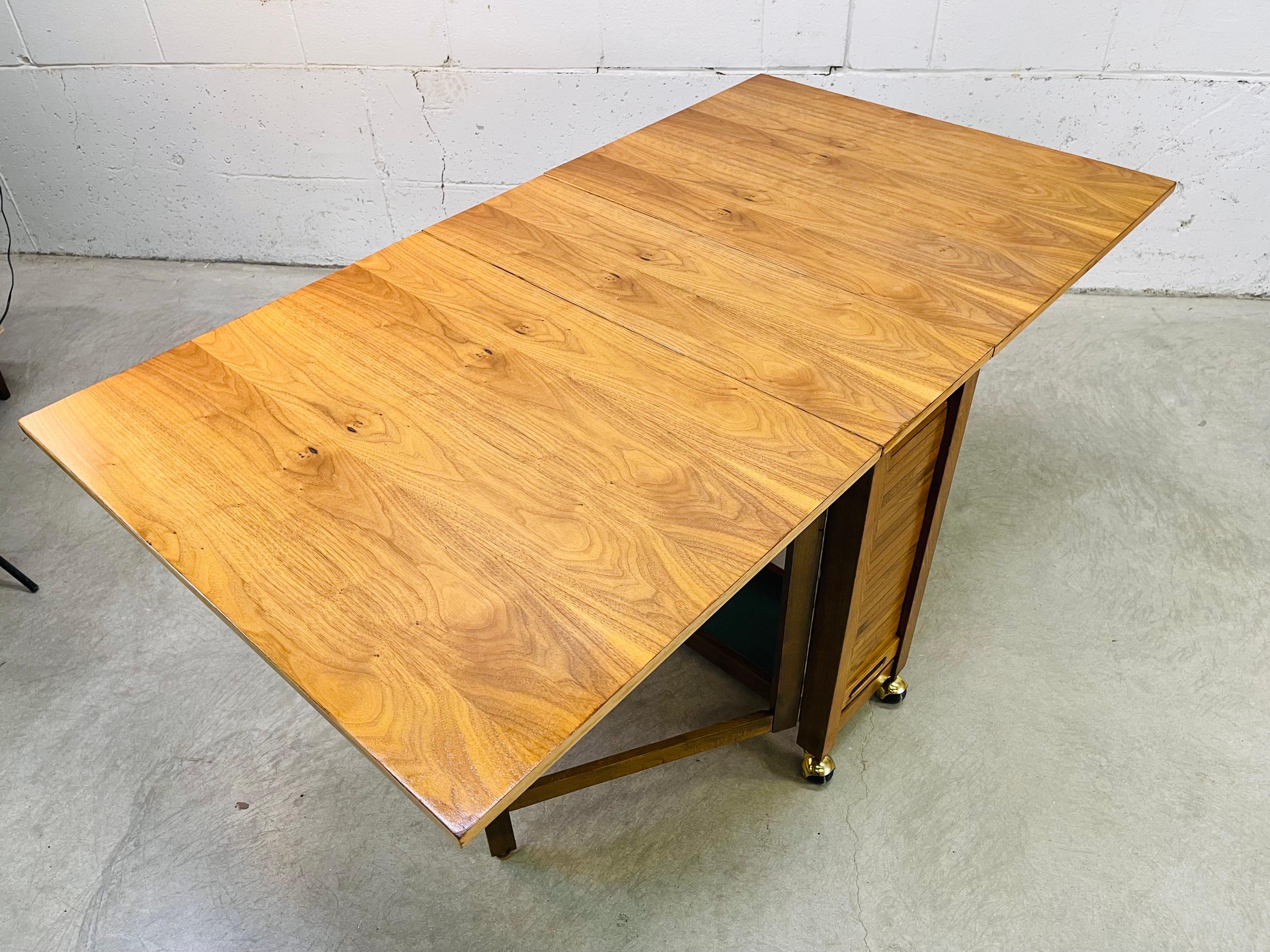 Vintage 1960s maple wood folding dining table with storage. This space savings table has a tambour side door that open to storage and would have held chairs. The chairs are not included. But this space could still be used for storage. The table