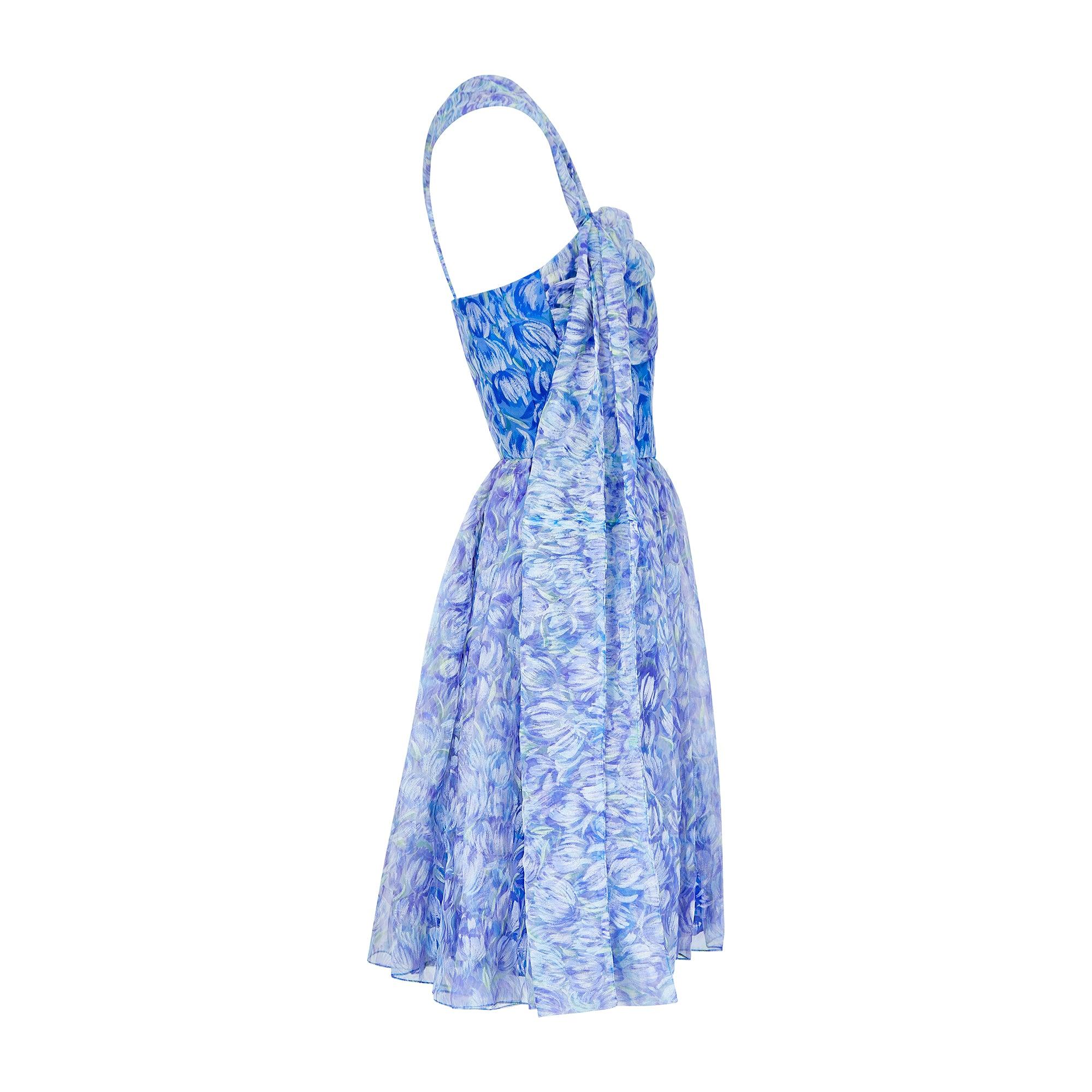Este bonito vestido fue diseñado por Marldena a finales de los años 50 y principios de los 60, y sería perfecto para un evento formal o una fiesta. El tejido, de corte generoso, es una gasa sintética lila transparente, estampada con tulipanes en