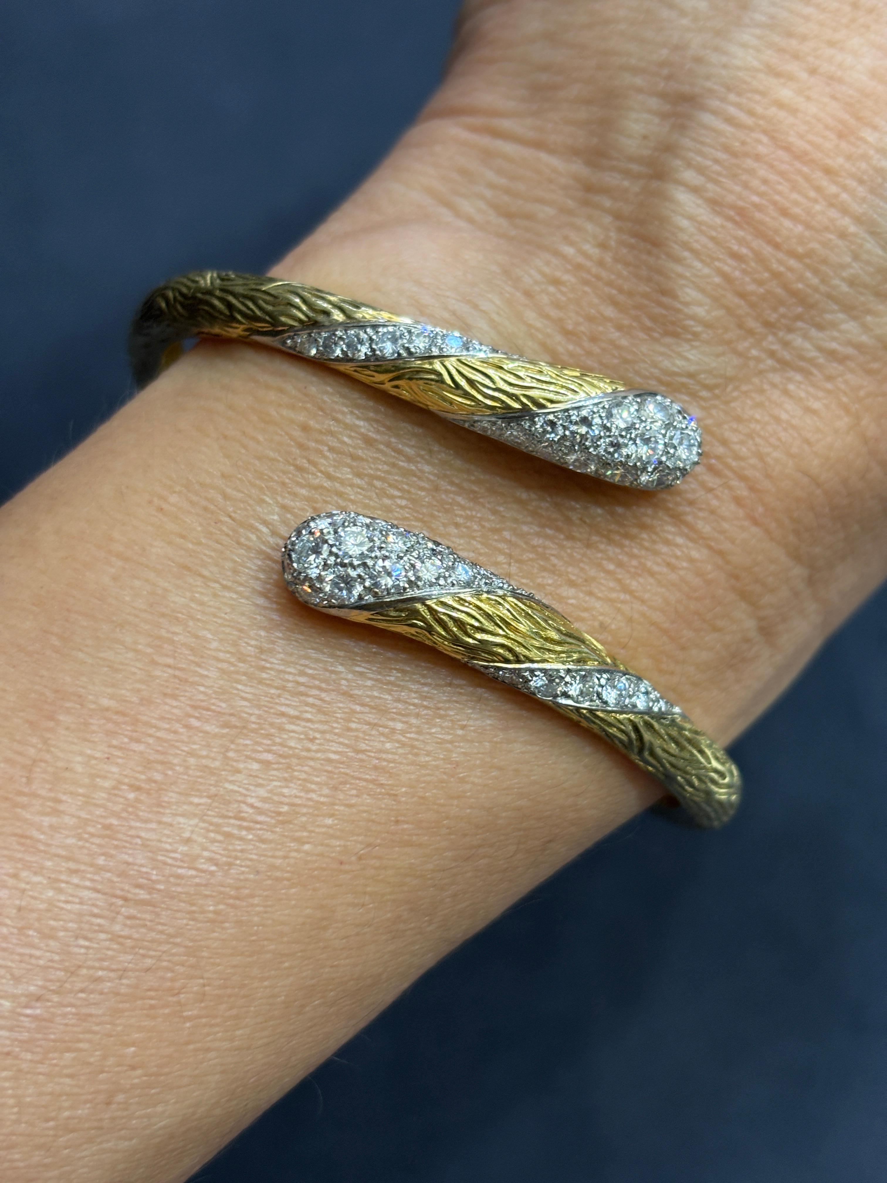 Questo elegante braccialetto asimmetrico di Mauboussin risale agli anni '60. Realizzato in oro 18 carati, il metallo è stato inciso e ornato con diamanti a taglio rotondo. Il braccialetto si apre grazie a una cerniera per far entrare la mano. La