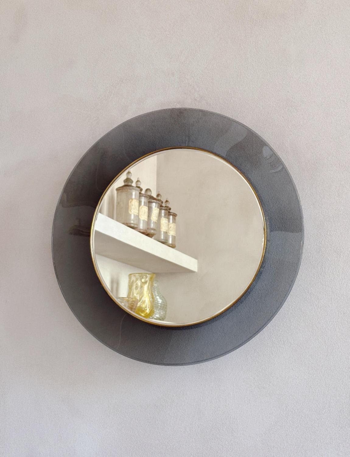 A stunning and rare example of a smokey grey circular glass mirror designed by Max Ingrand and made by Fontana Arte in 1966. The mirror is surrounded by a conclave glass frame in smokey grey. The model number for this historic design piece is 1669