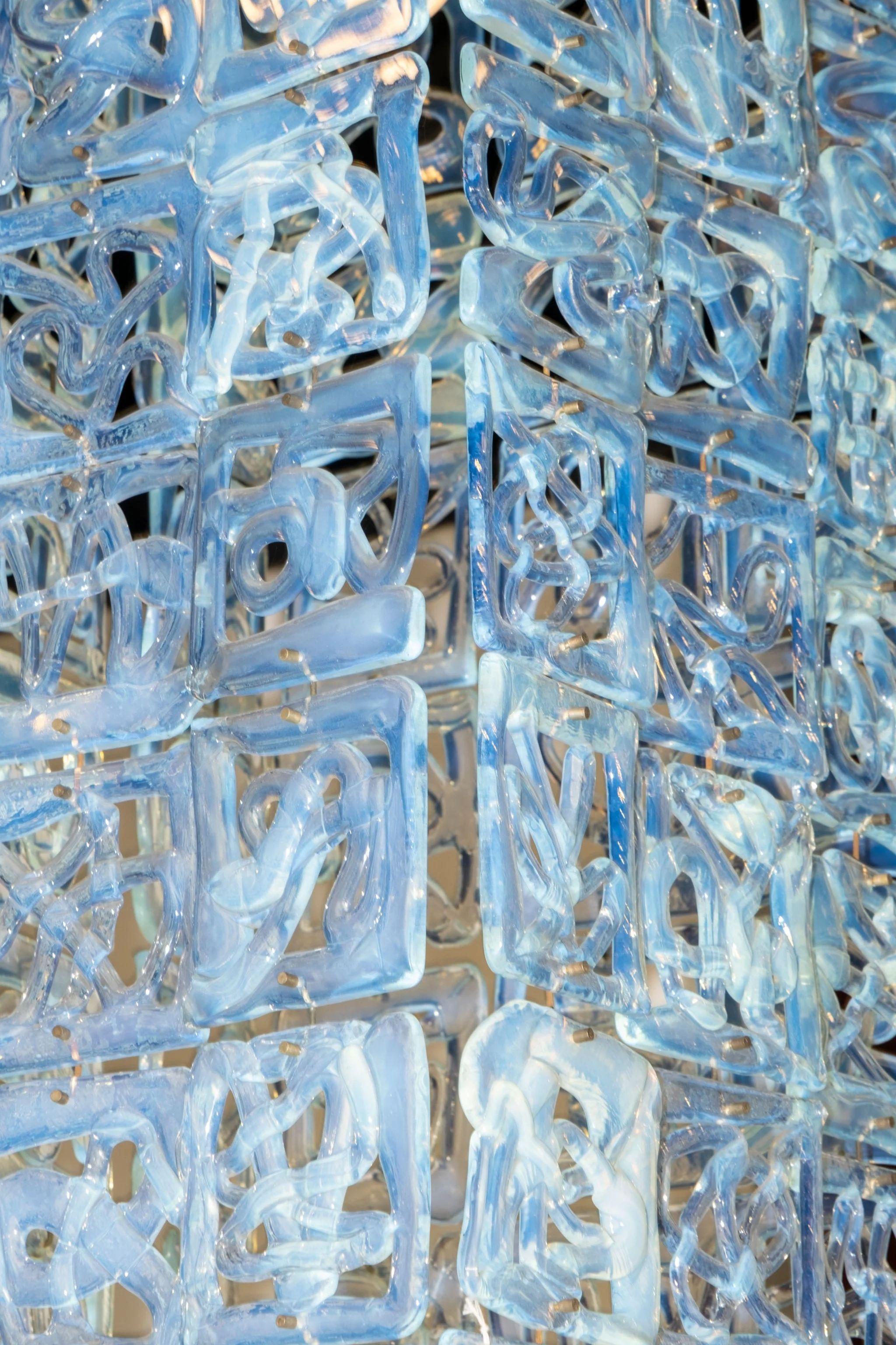Disegnato da Carlo Nason per Mazzega negli anni '60, questo lampadario in vetro di Murano sovrappone tessere di vetro opalino in una colonna di luce ipnotica. Ogni pannello formato a mano presenta texture vorticose che catturano e disperdono il