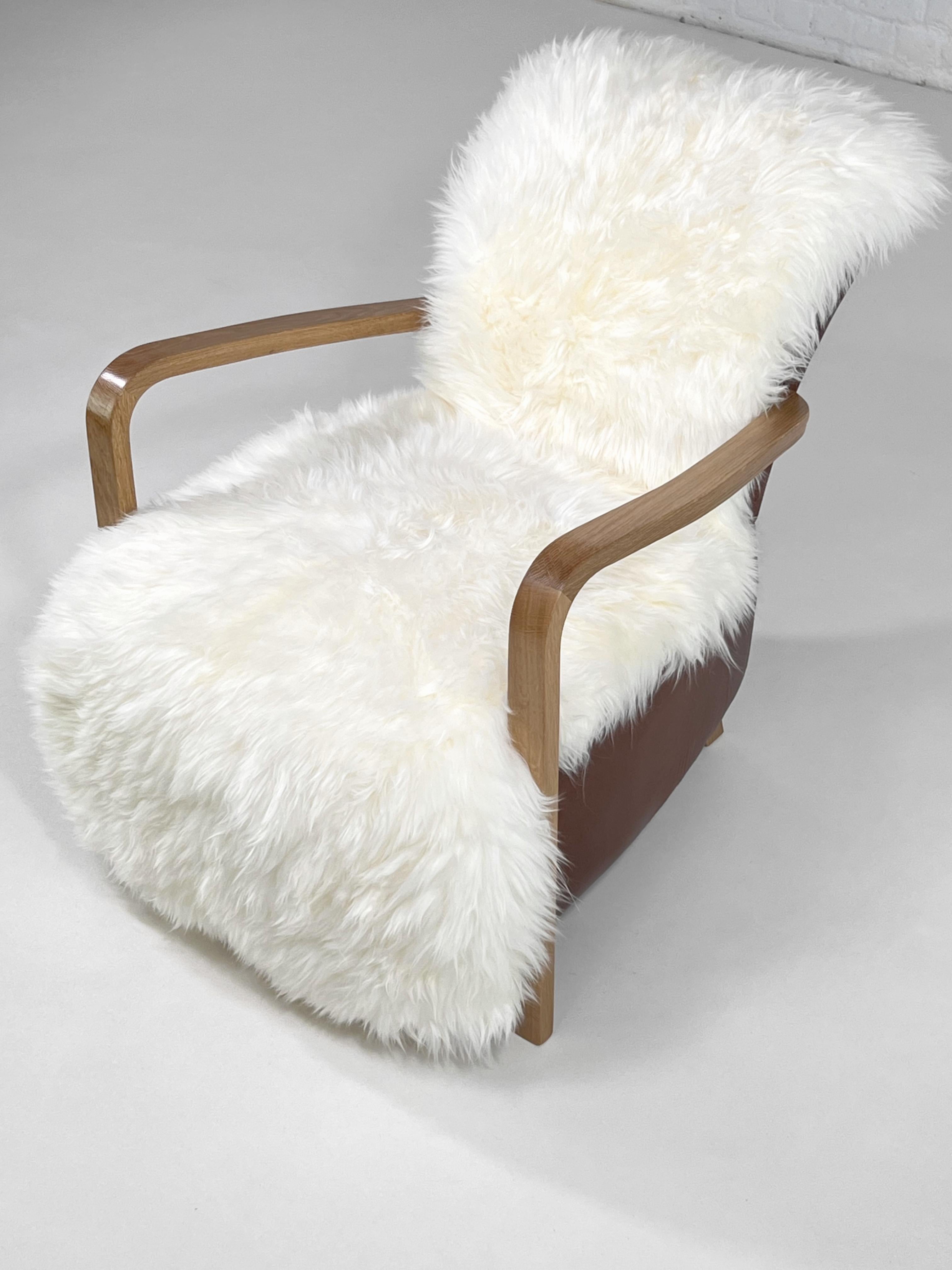 1950s - 1960s MCM Design Scandinavian Style Wooden And Cognac Leather Lounge Armchair With Sheepskin seat composed of a natural wooden feet which the front one make the armrests and a comfy seat in white sheepskin with cognac leather back.