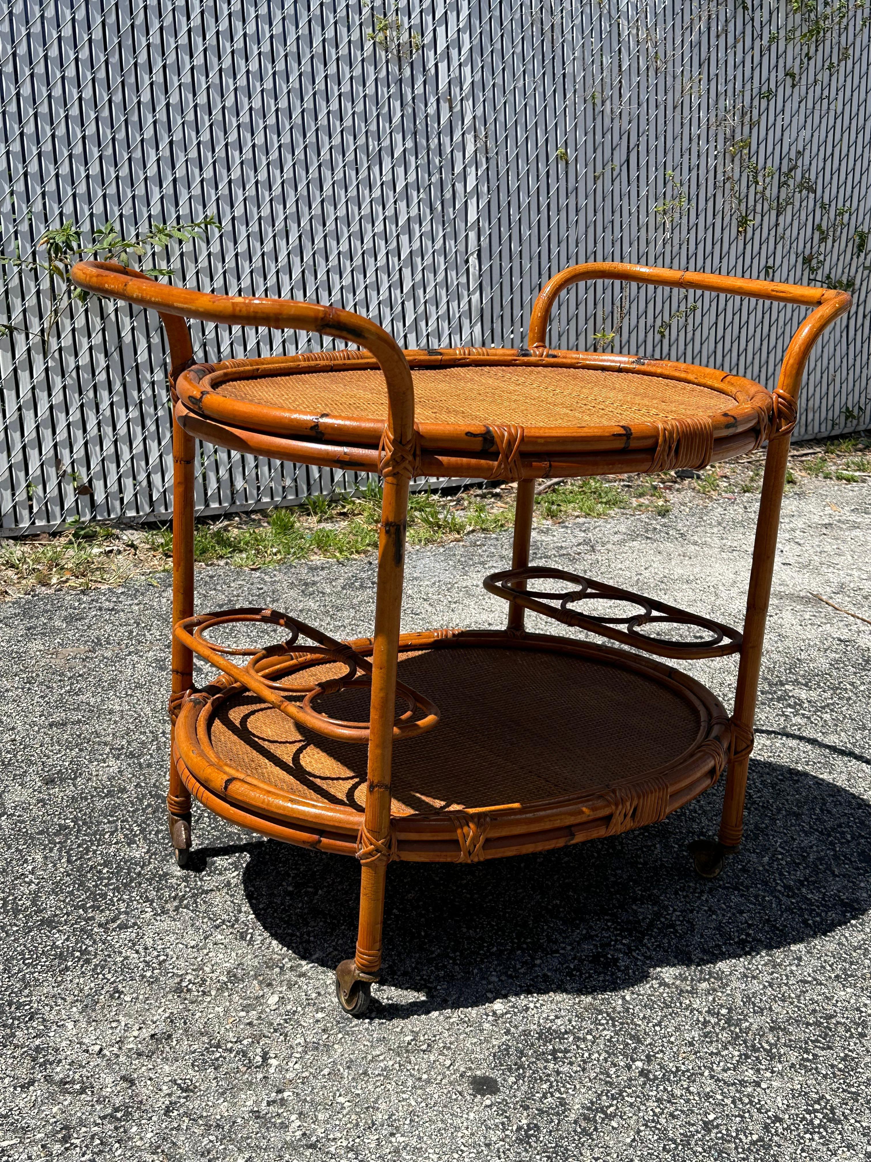 Gorgeous midcentury rattan and bamboo cane oval bar cart with four brass wheels. This fantastic piece was designed in Italy during the 1960s.  A stunning serving bar cart in fantastic vintage condition. It features two oval shelves with woven rattan