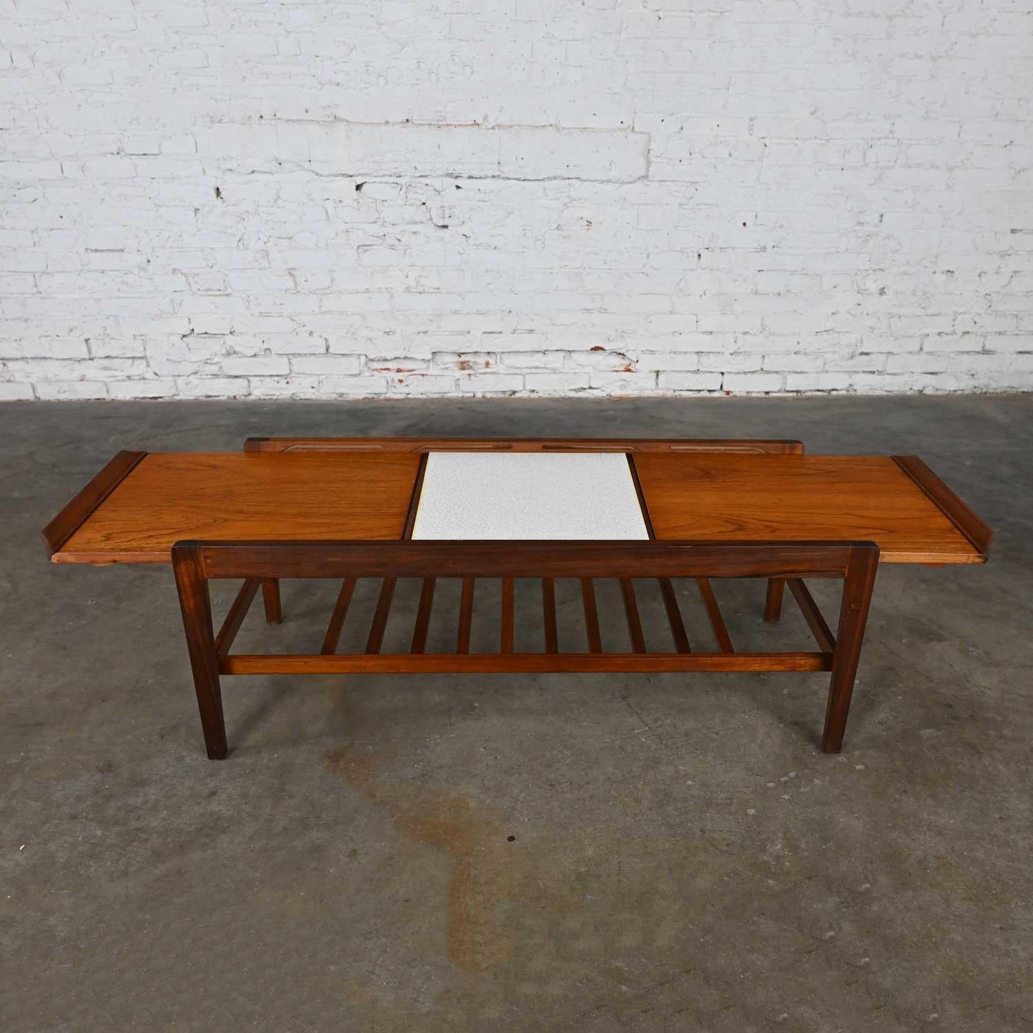 Handsome vintage MCM Scandinavian Modern style teak extending coffee table with sliding top, white Formica square center with gold leaves, and a lower slatted shelf. Beautiful condition, keeping in mind that this is vintage and not new so will have