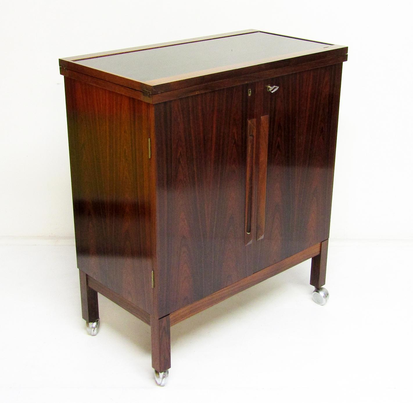 A 1960s Norwegian rosewood metamorphic dry bar cabinet by Torbjorn Afdal for Bruksbo.

In Rio rosewood with brass detail and black melamine surface, this compact drinks cabinet transforms into a full size bar. 

It can be used in its compact
