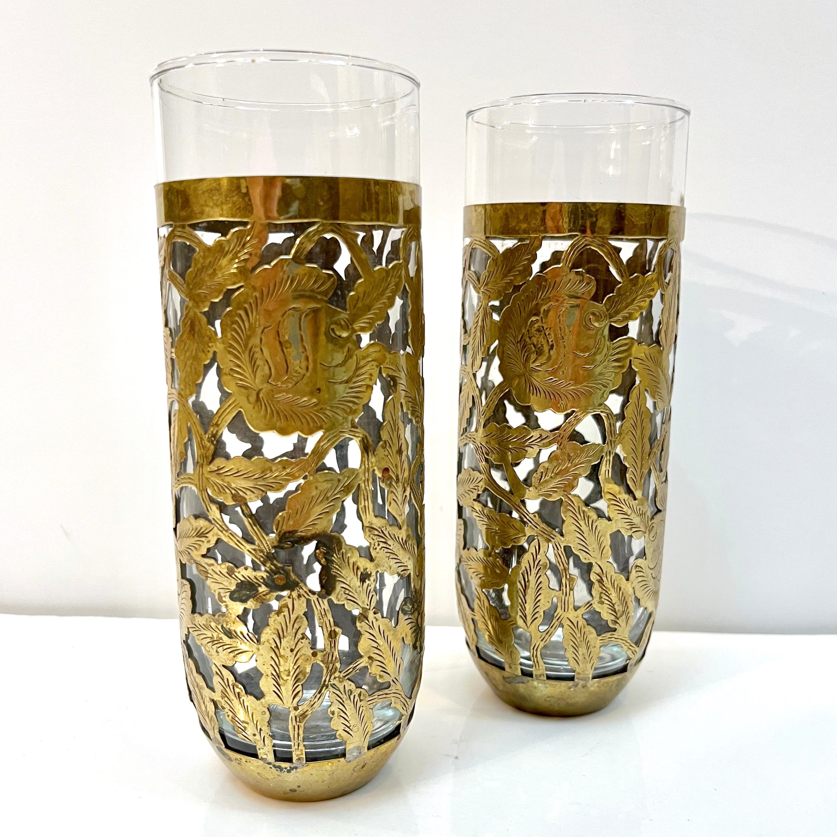 1960s mid-20th century pair of organic glasses, entirely handcrafted in Mexico, overlayed in a handmade antique brass open sheath ornate with an etched cutwork floral and foliage decor.
Ideal as barware but also as individual vases for floral