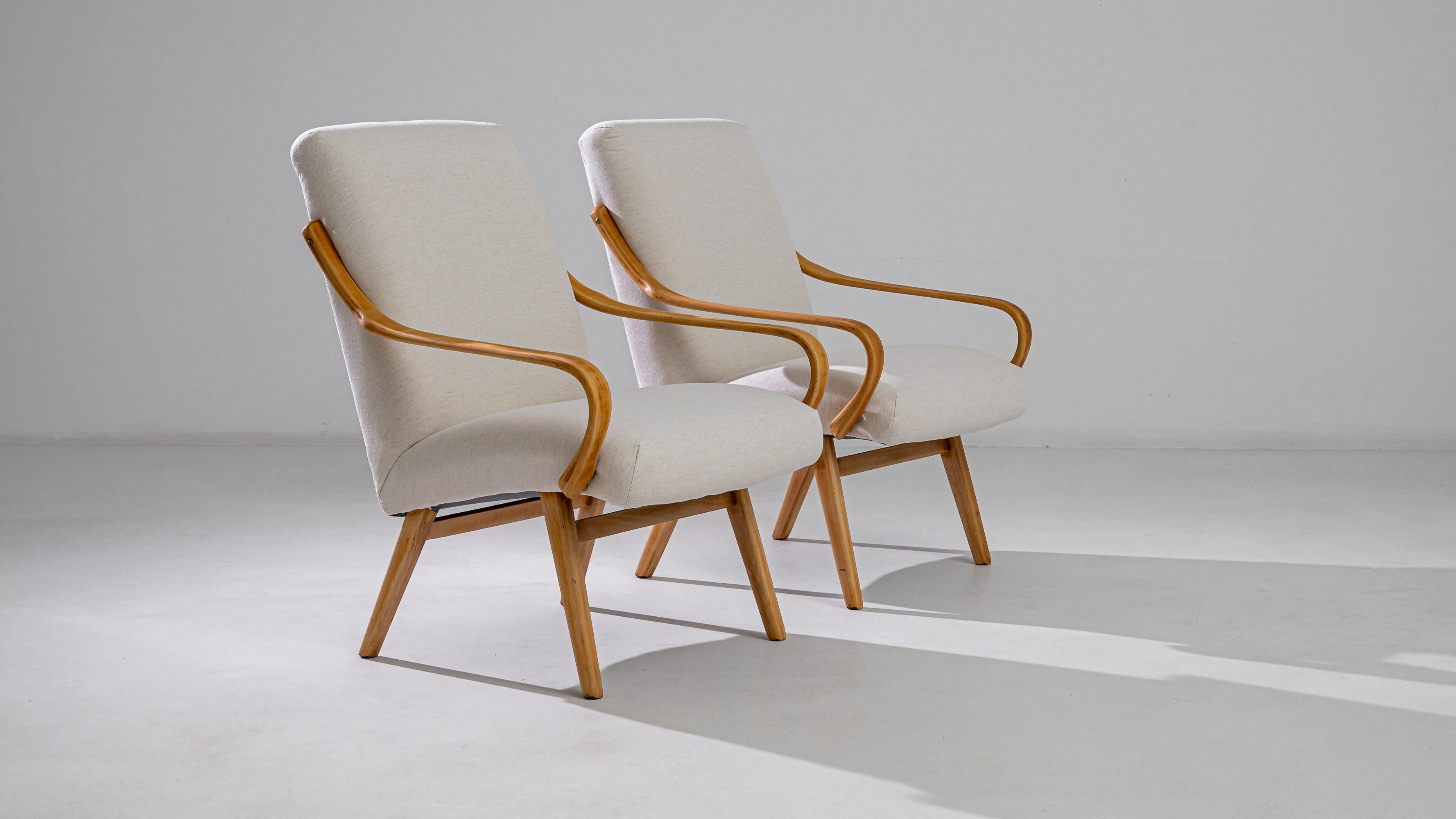 Produced in the former Czechoslovakia, this pair of armchairs from circa 1960 are re-upholstered with an updated natural white fabric, chosen to compliment the elegant polish of the hardwood frame. Comfortable angles and clean lines are designed to
