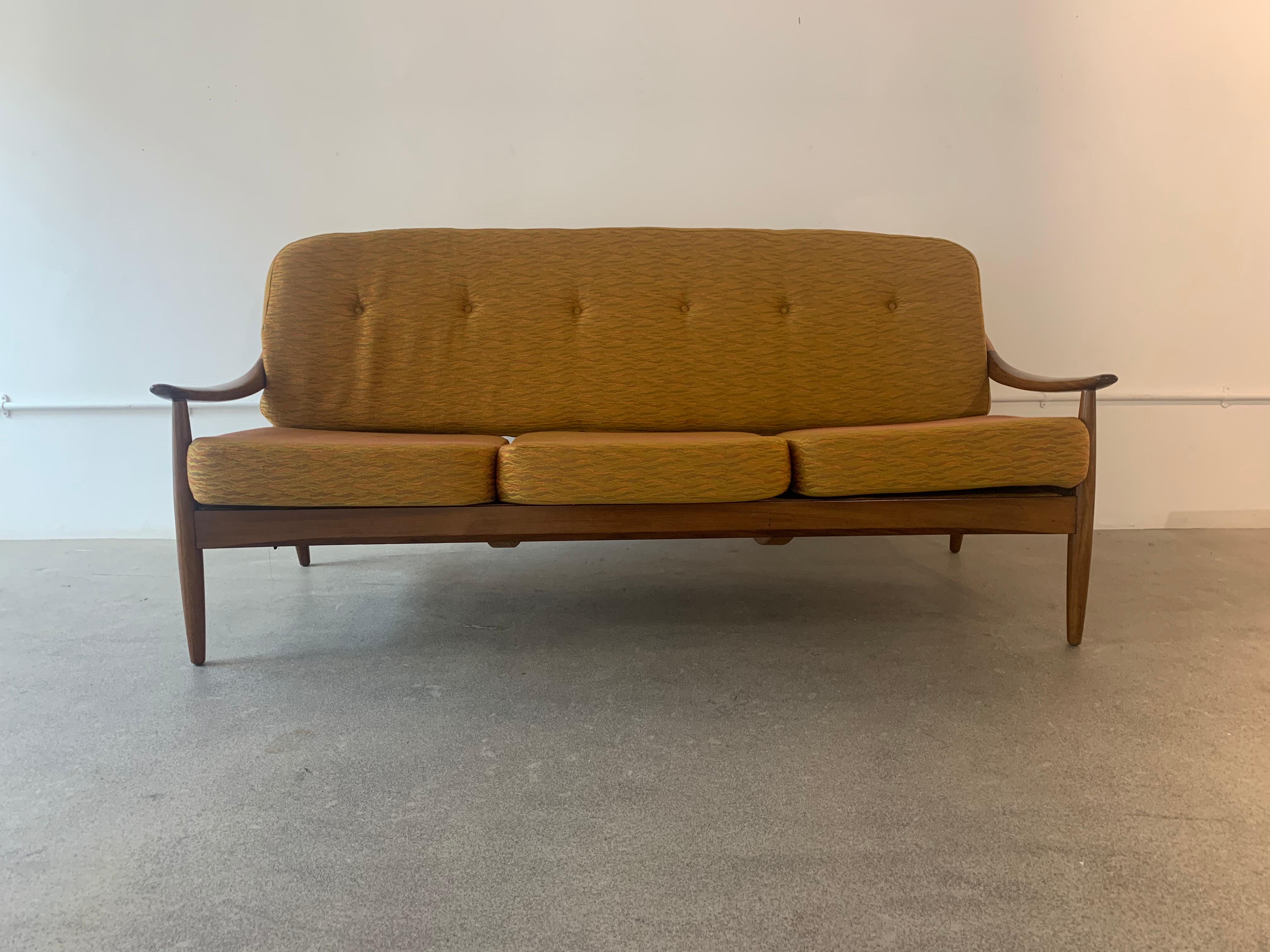 1960s Greaves and Thomas teak bentwood sofa. The sofa is formed from steam bent solid teak with curved sweeping armrests, a spindle back with turned, tapered, flared legs. The seat and buttoned back cushion are upholstered in a flame orange and gold