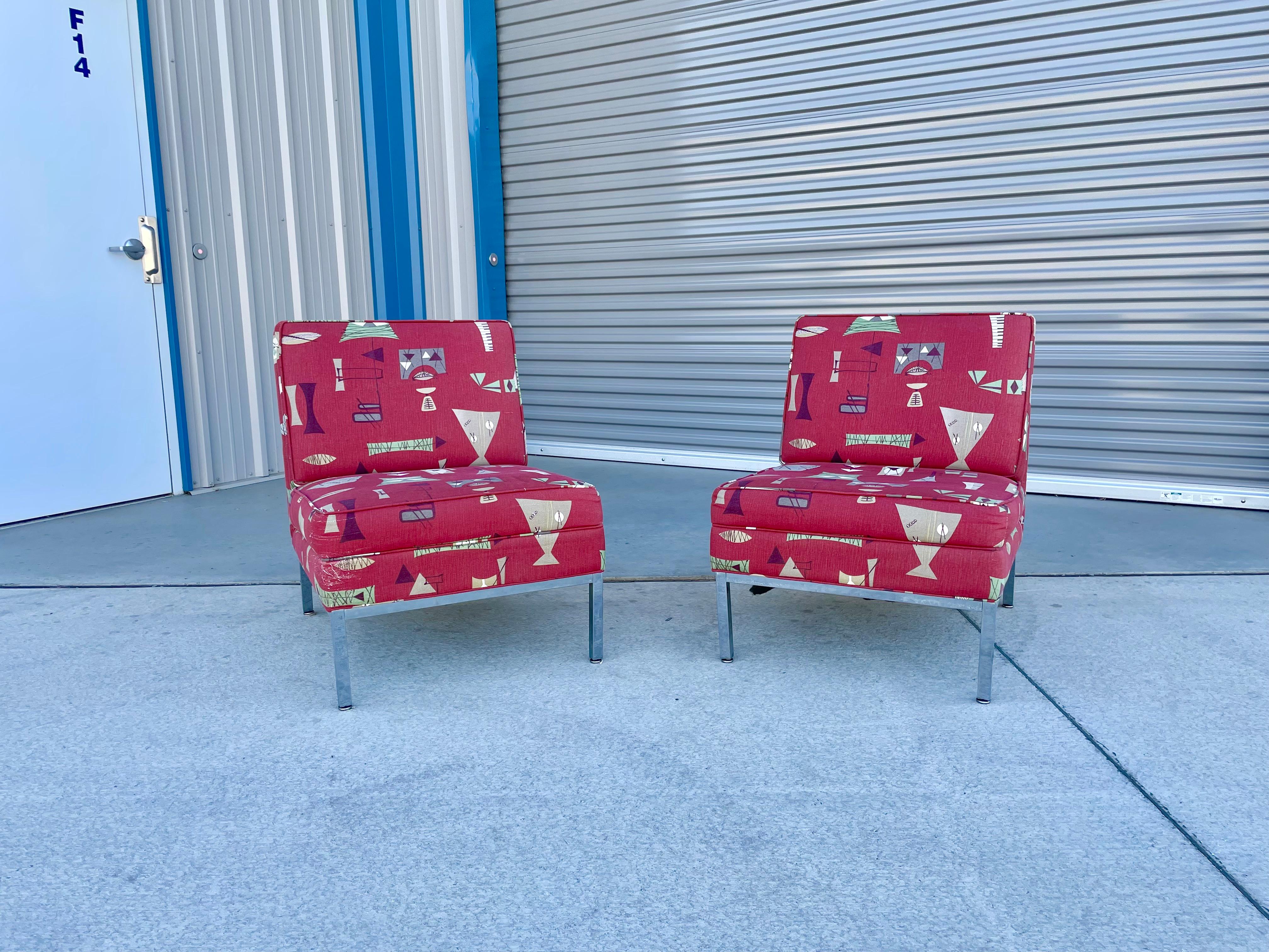 Mid-century chrome lounge chairs that were designed and manufactured in the United States during the 1960s. These chairs are styled after Florence Knoll. These chairs feature a red upholstery that sits on top of a chrome frame, making them the