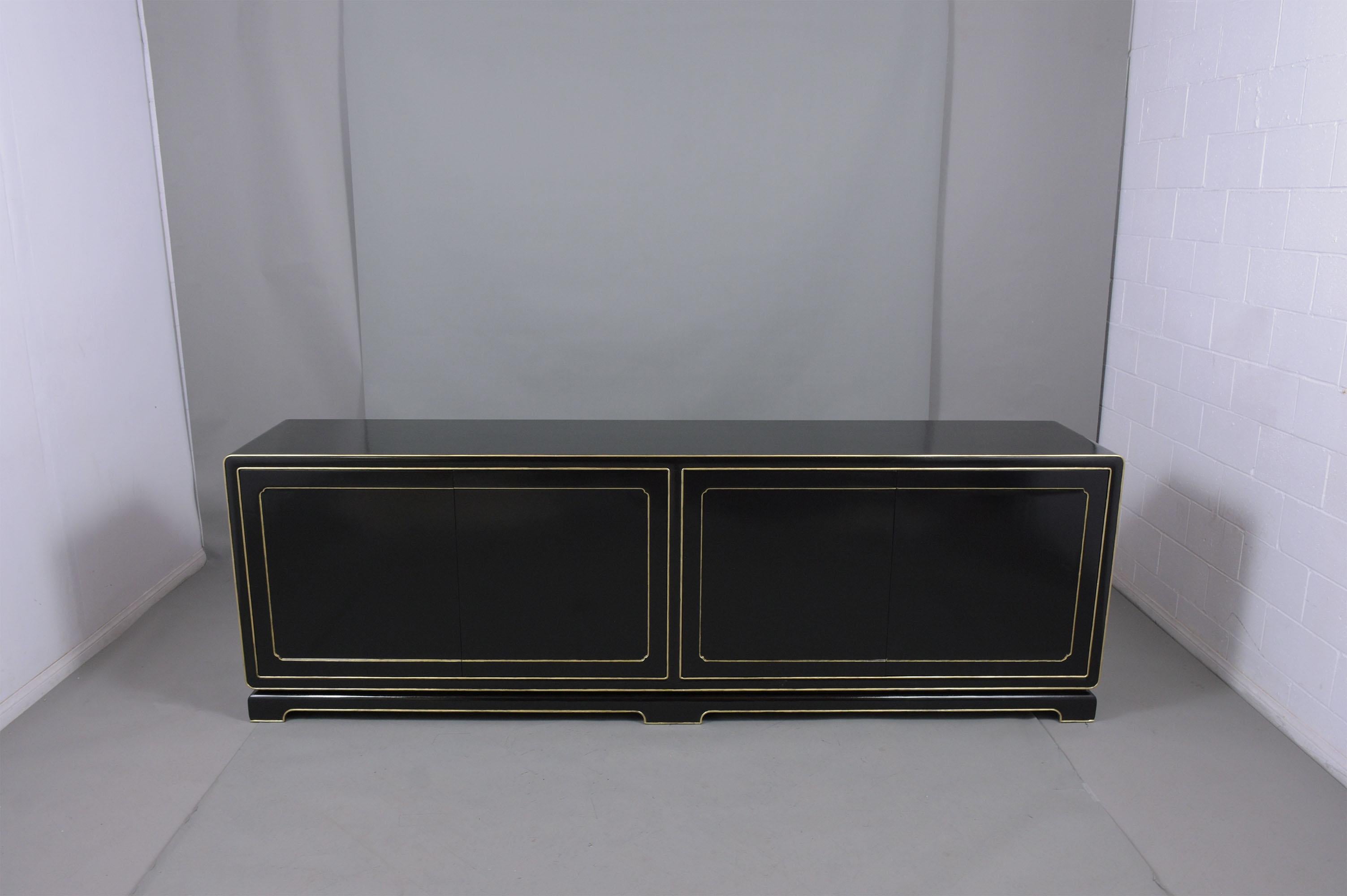A sleek mid-century modern ebonized credenza is handcrafted out of mahogany wood stained in an elegant ebonized color with gilt molding details and a newly lacquered finish by our team of expert craftsmen. This fabulous vintage buffet has four push